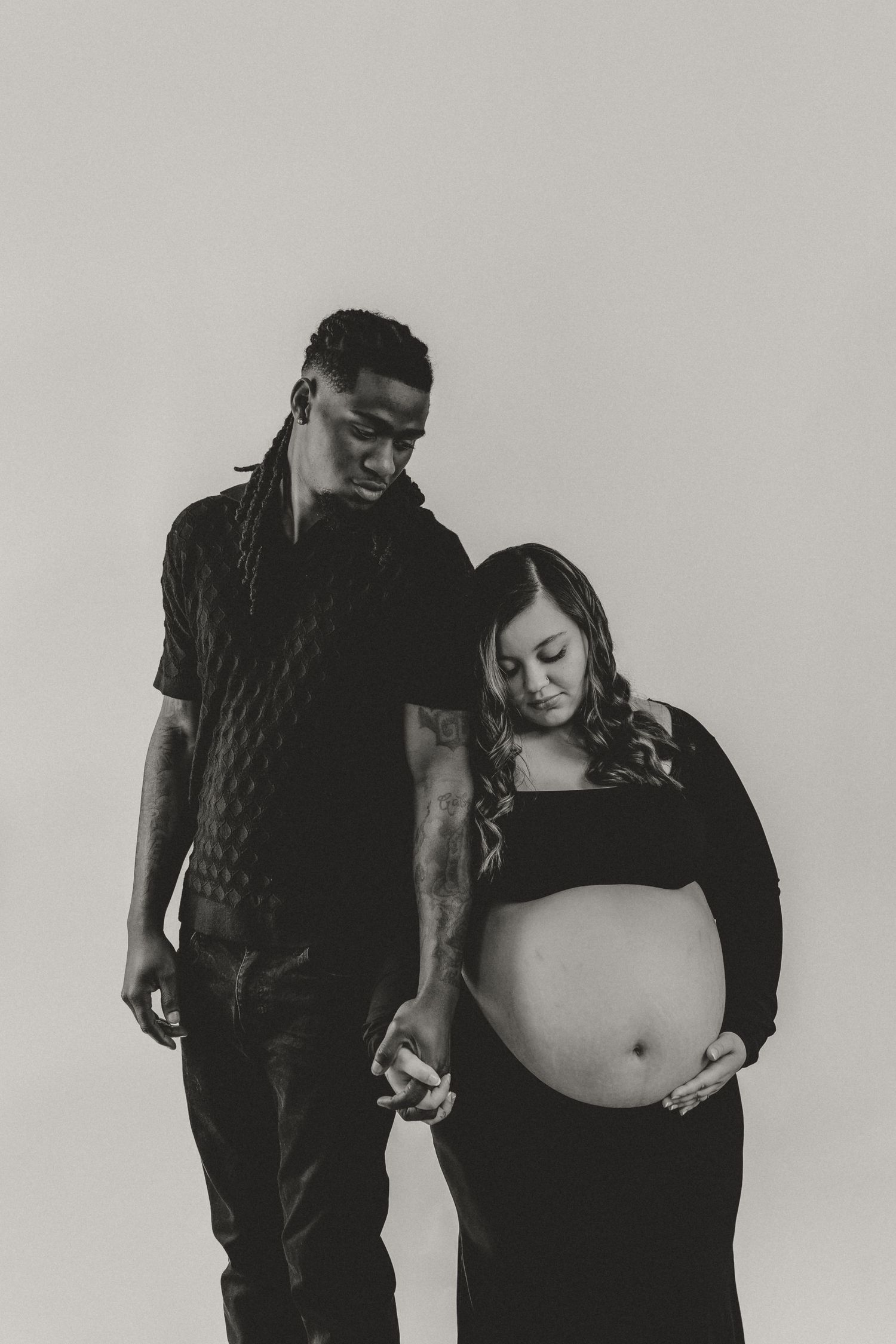 Expecting parents hold hands and cradle into each other to document a photo during their maternity session in Bloomington, IL
