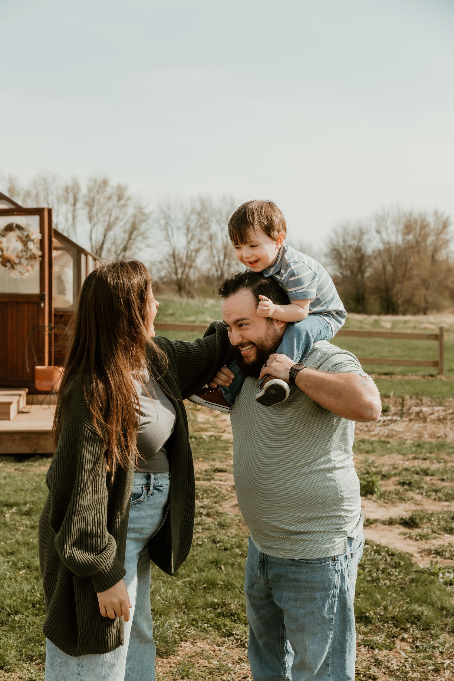 Father has son on his shoulders while mom tries to get him to laugh during a playful moment captured by central il photographer