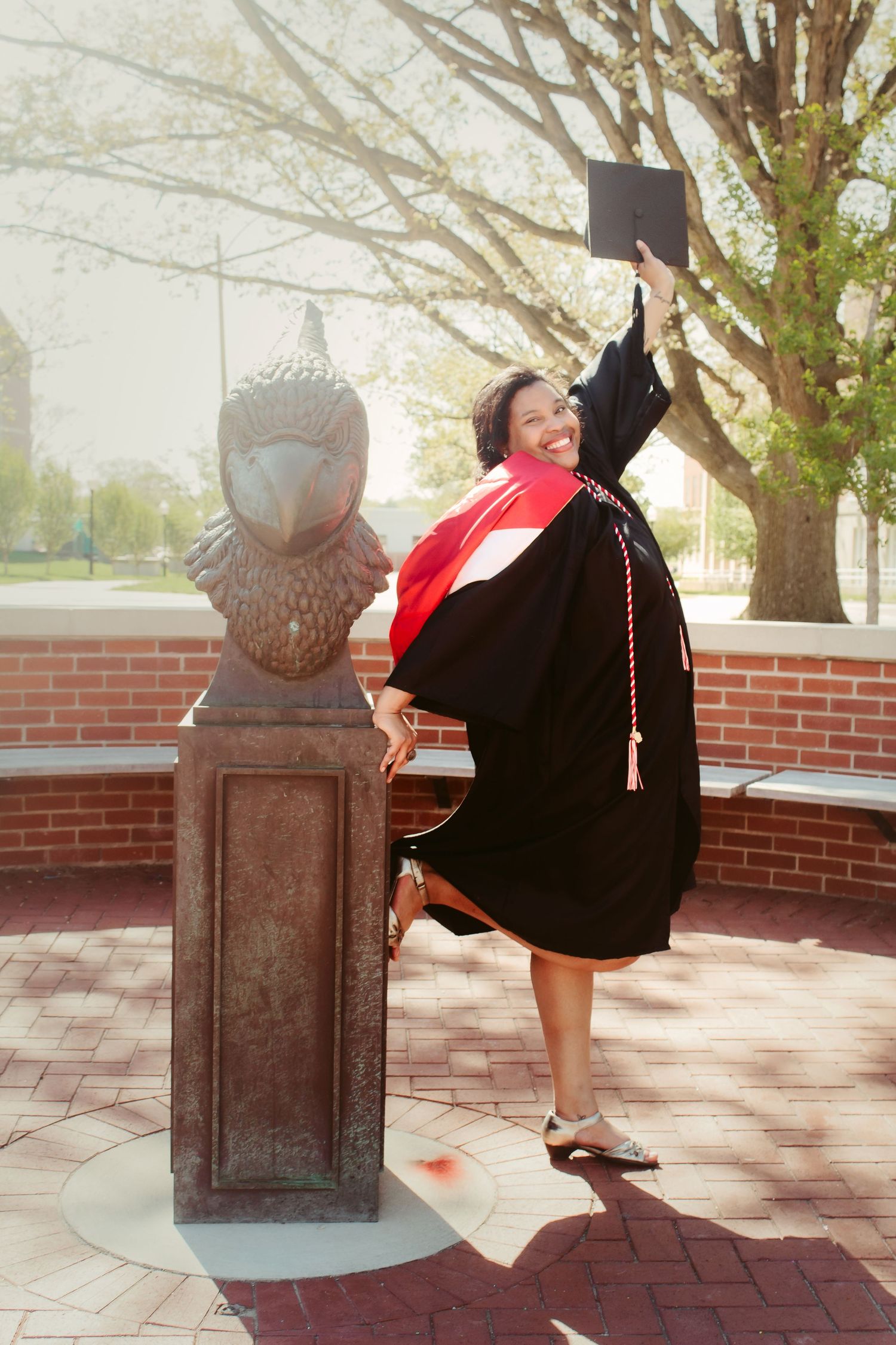 Senior graduating college holds cap in the air while leaning on ISU redbird statue captured by central il senior photographer