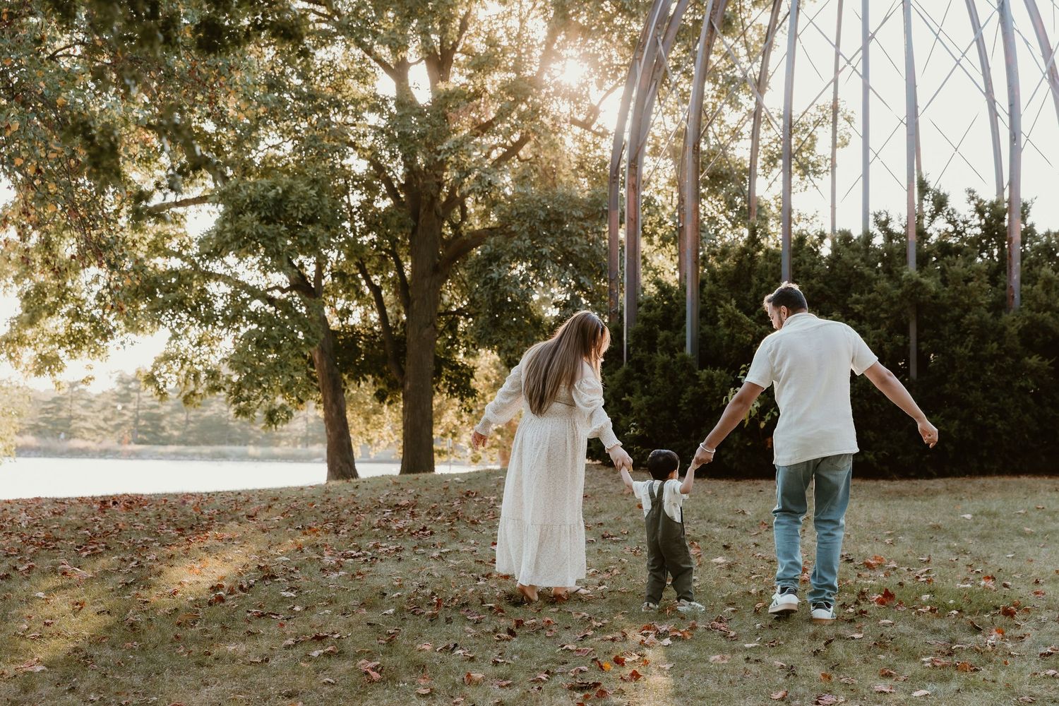 Mom and Dad hold their sons hand during a golden hour family session at Miller Park with central illinois family photographer