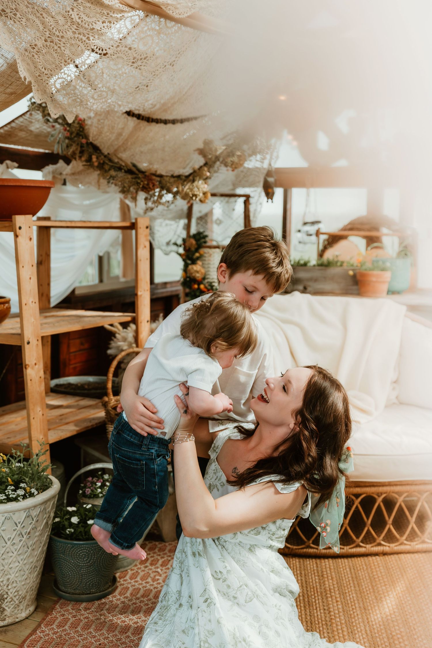 Mother holds child in the air above while her other child hugs into them during a sweet moment captured by bloomington illinois photographer