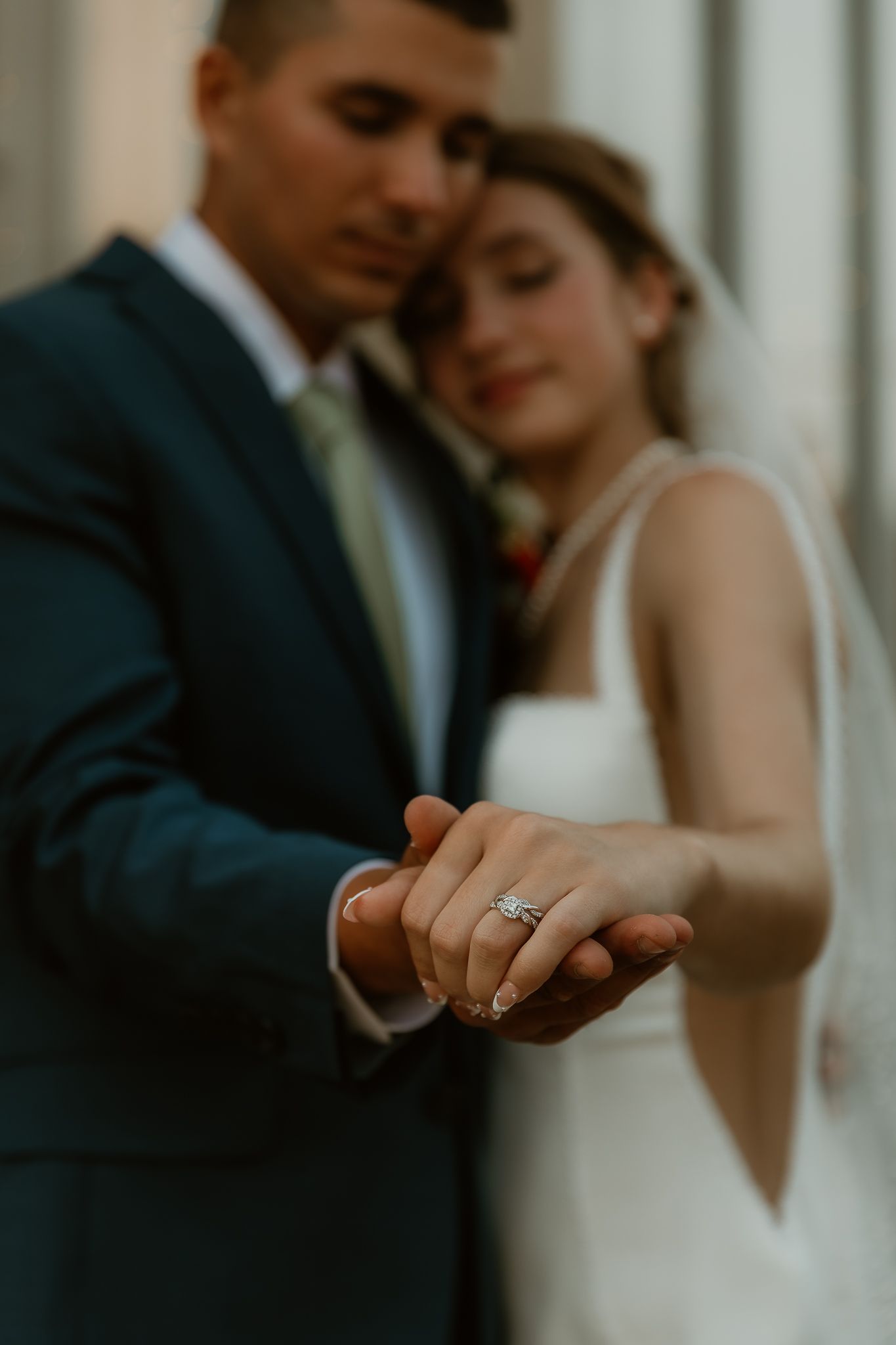 Bride and Groom share a cuddle and show off her wedding rings during couple's wedding portraits