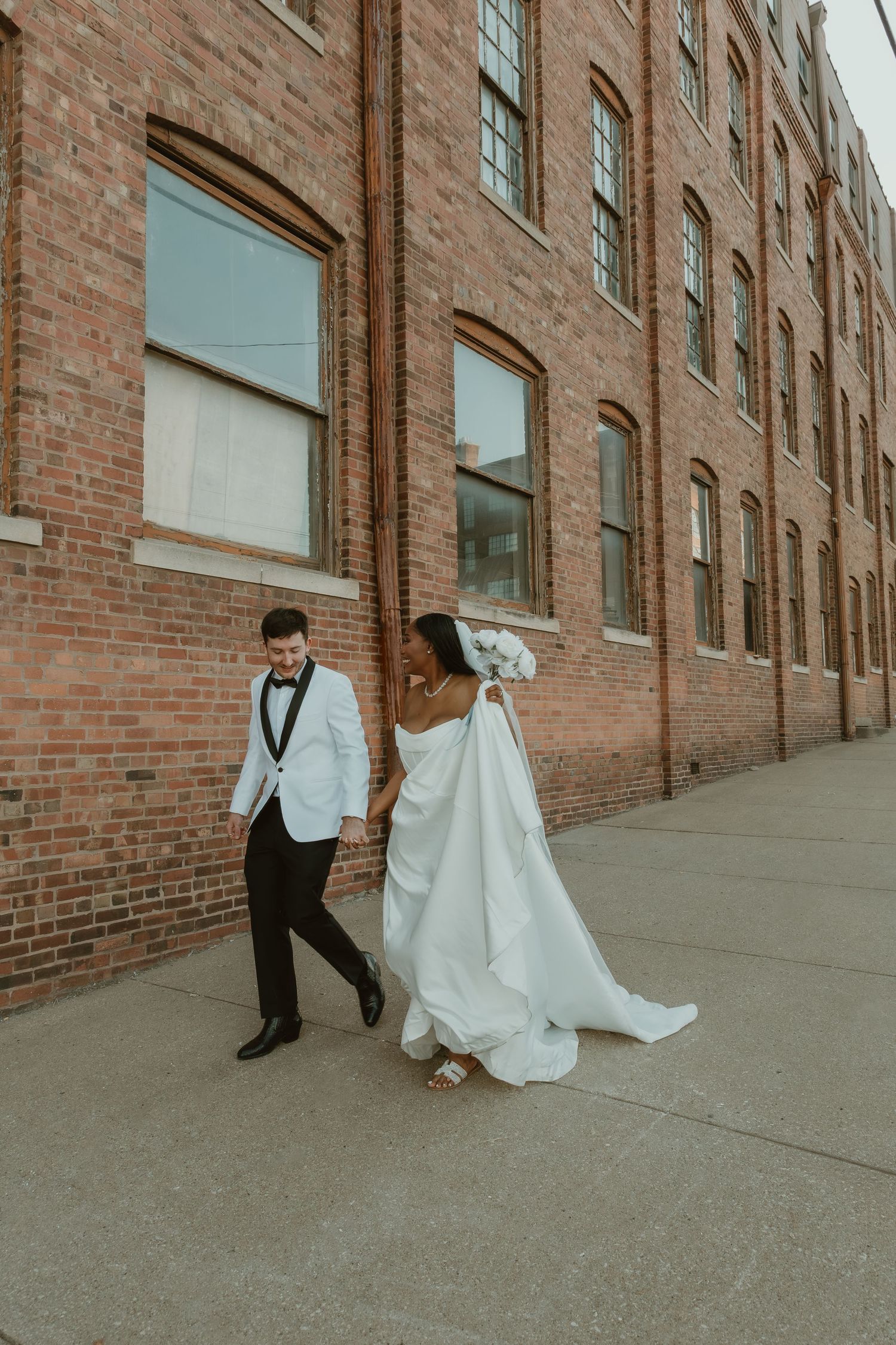 Bride and Groom captured during wedding portraits walking down a sidewalk in Peoria warehouse distract