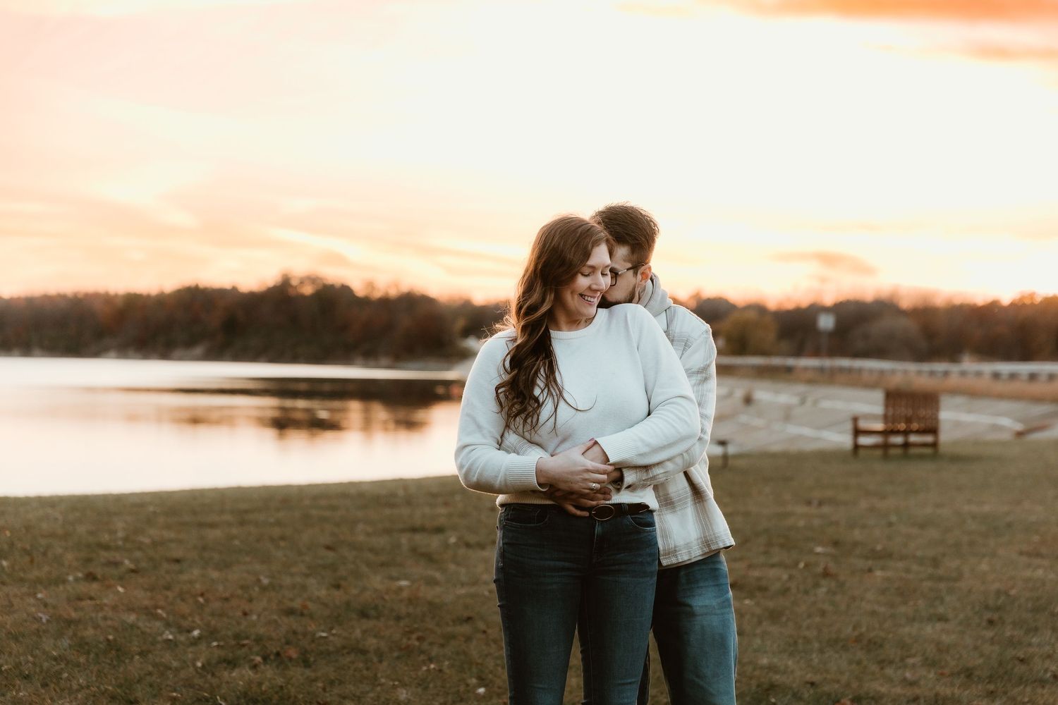 Couple cuddling with eachother in front of the lake during sunset