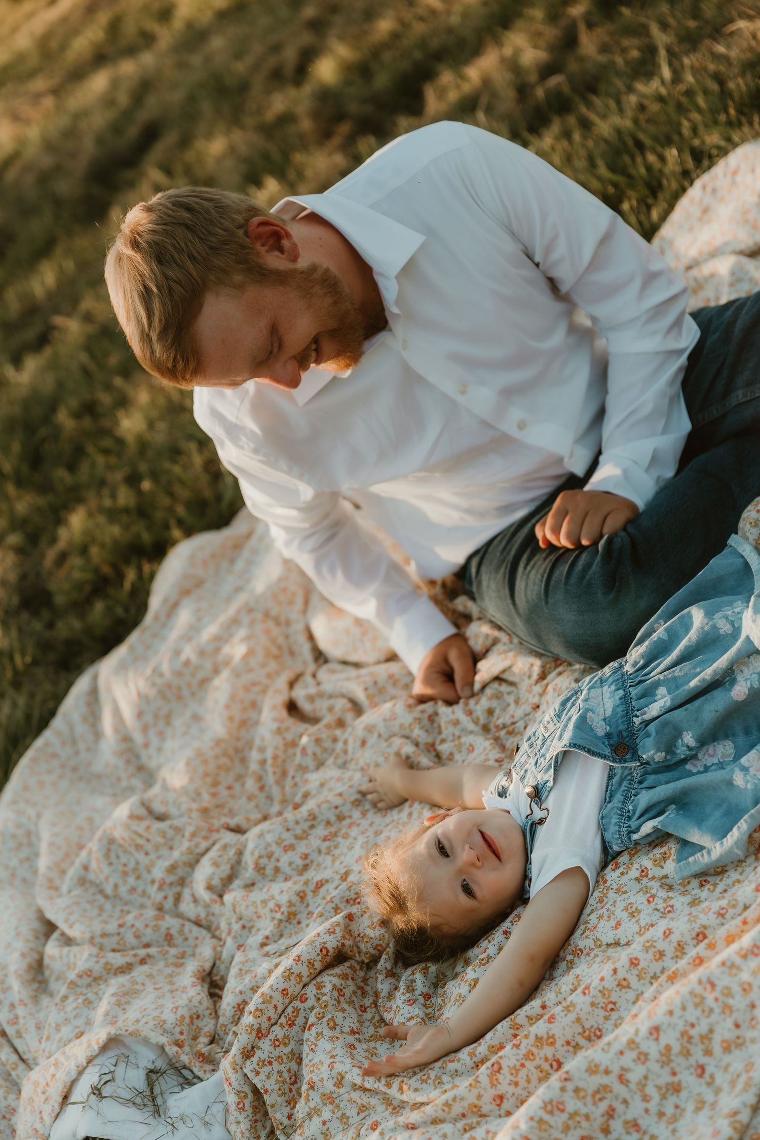 Dad and daughter cuddle and giggle on a blanket during golden hour in Bloomington, IL during a photo session