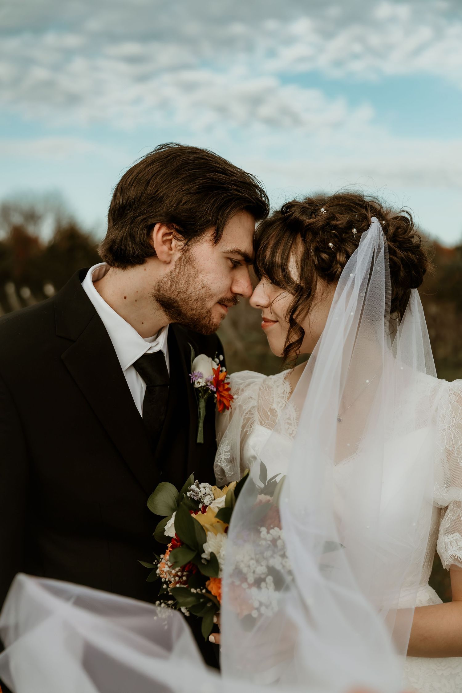 Bride and groom touching foreheads with a flowing veil in the wind