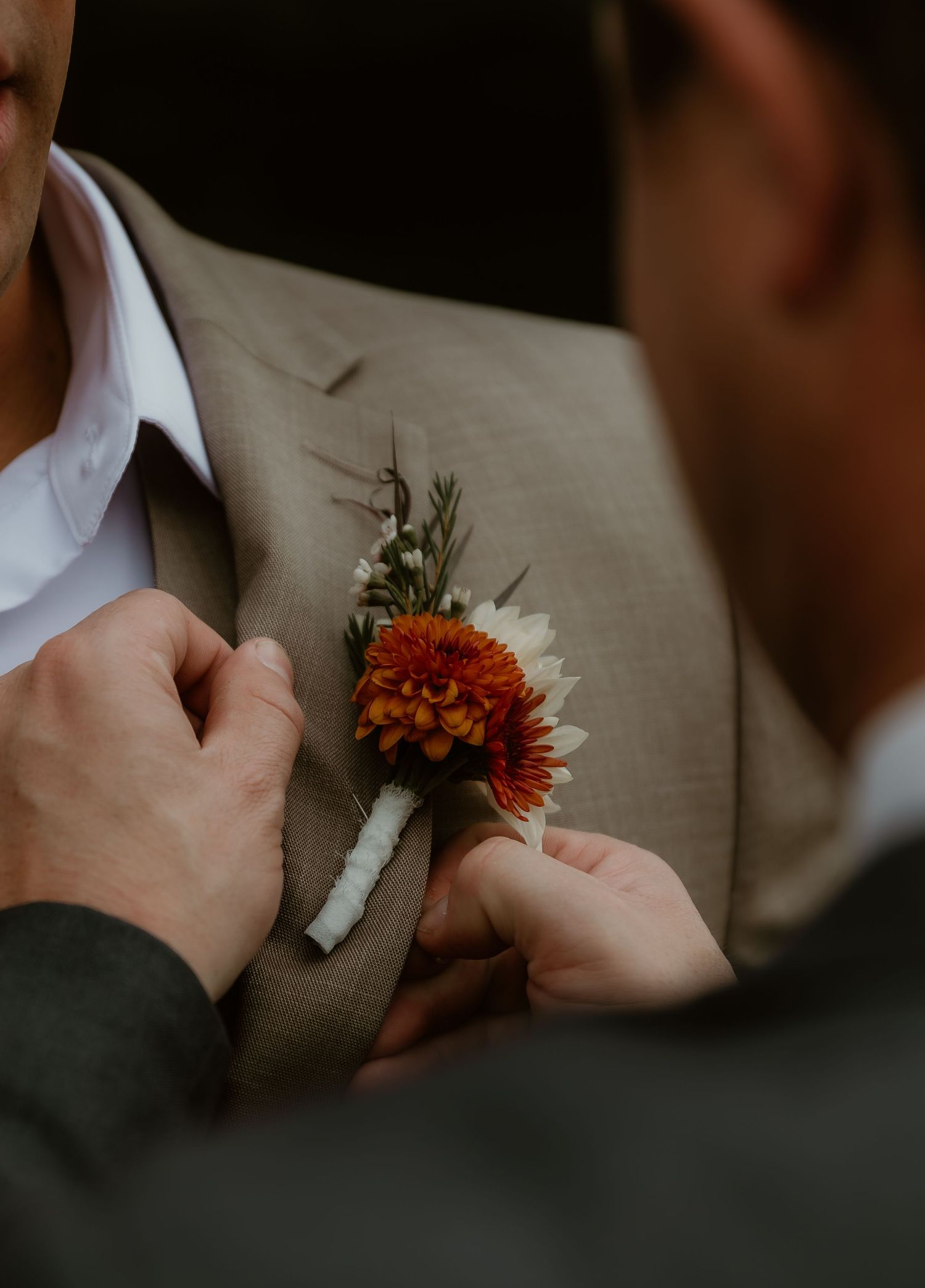 Best man helps groom put on his boutonniere during getting ready moments