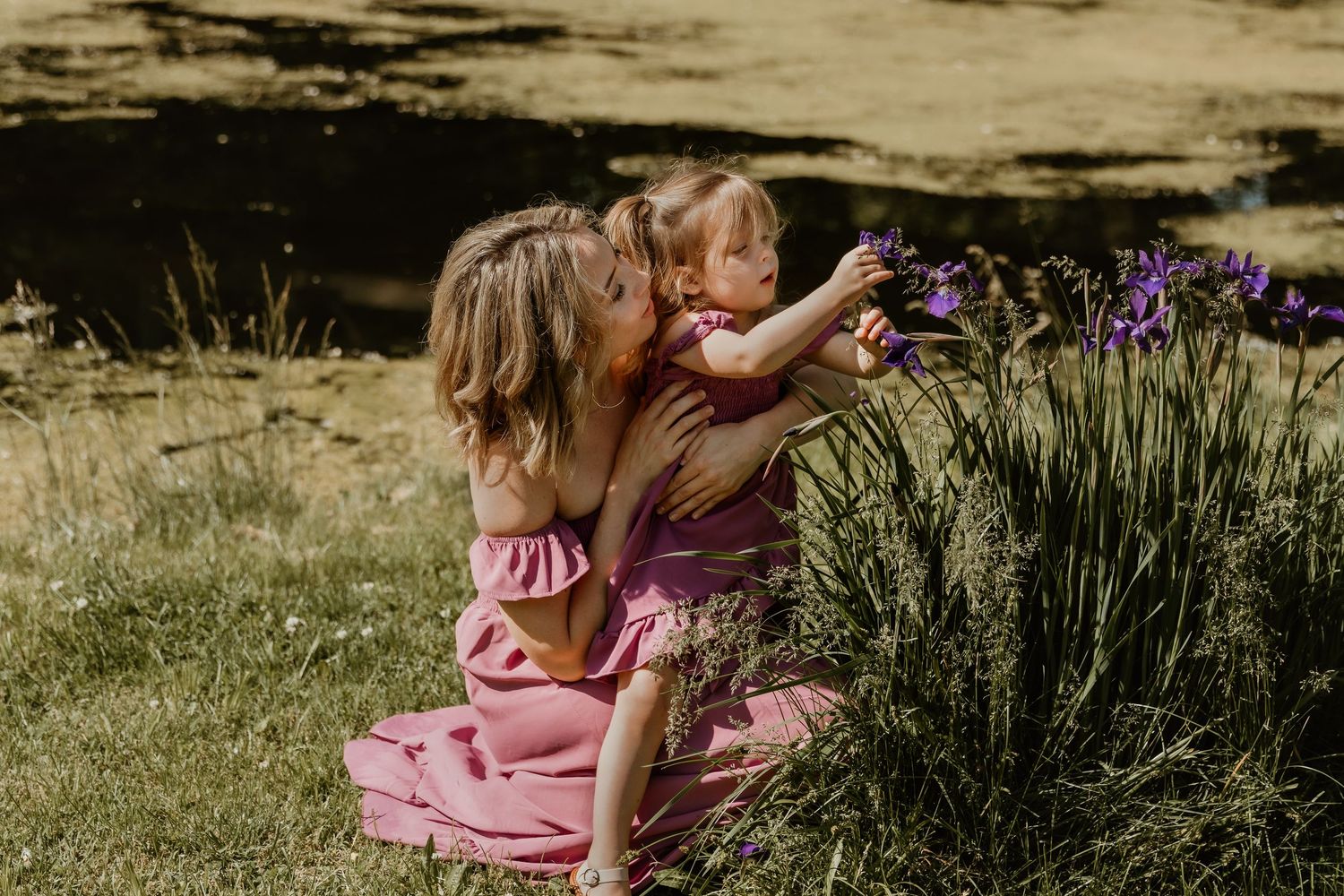 Mom and daughter sit by flowers while they take turns smelling each flower