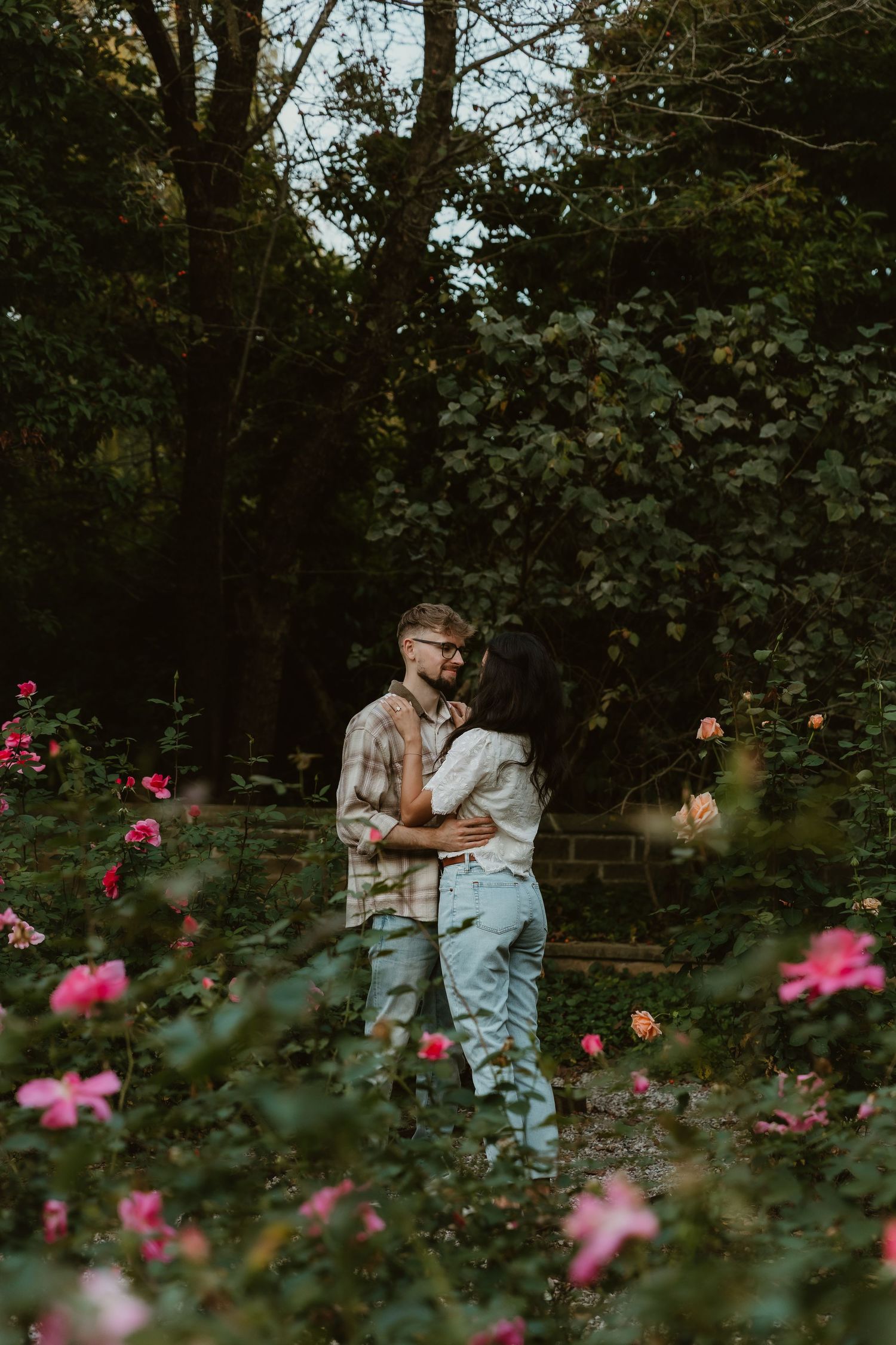 Romantic photo of a couple, surrounded by a rose garden, sharing an intimate moment with each other during their engagement photos