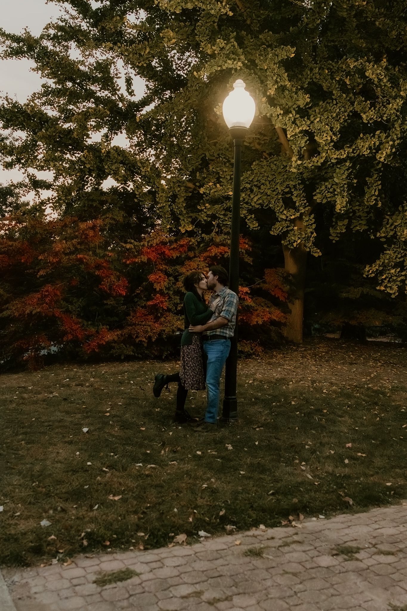 Couple kissing and leaning on a light pole under the evening sky