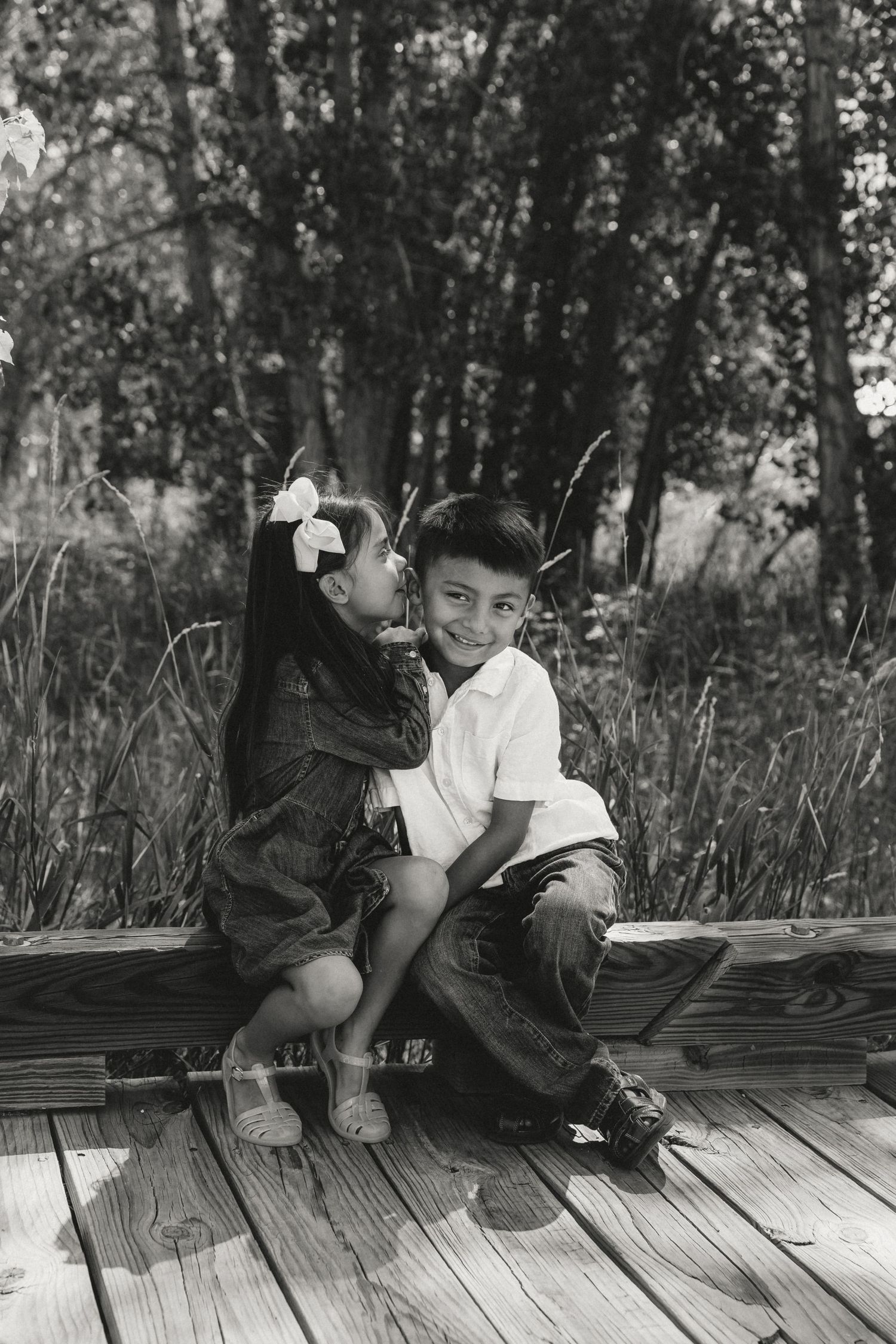 Sibling whispers in her siblings ear during a family session in Greeley, Colorado