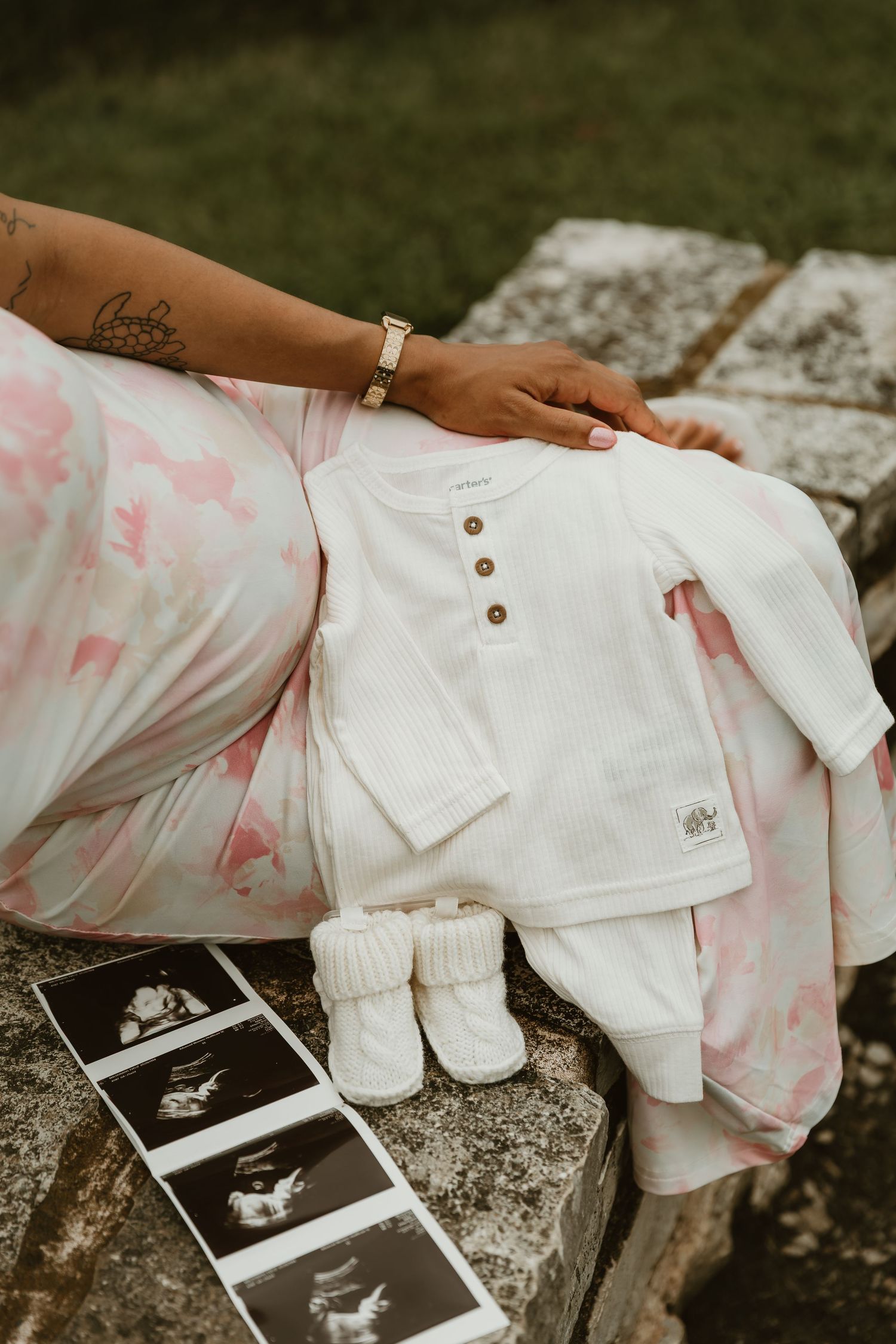 Expecting mother holding her daughters onesies while positioned by a sonogram for a maternity photo session