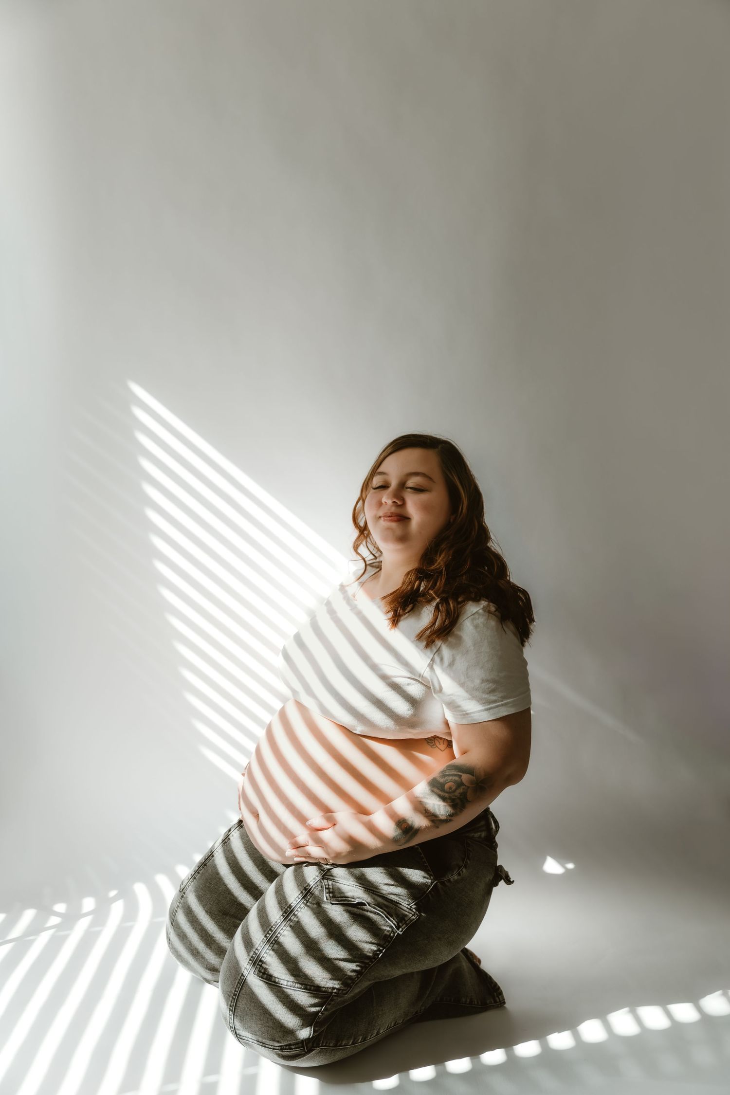 Expecting mother holds her belly in a natural lit area during a maternity session in Bloomington, Illinois