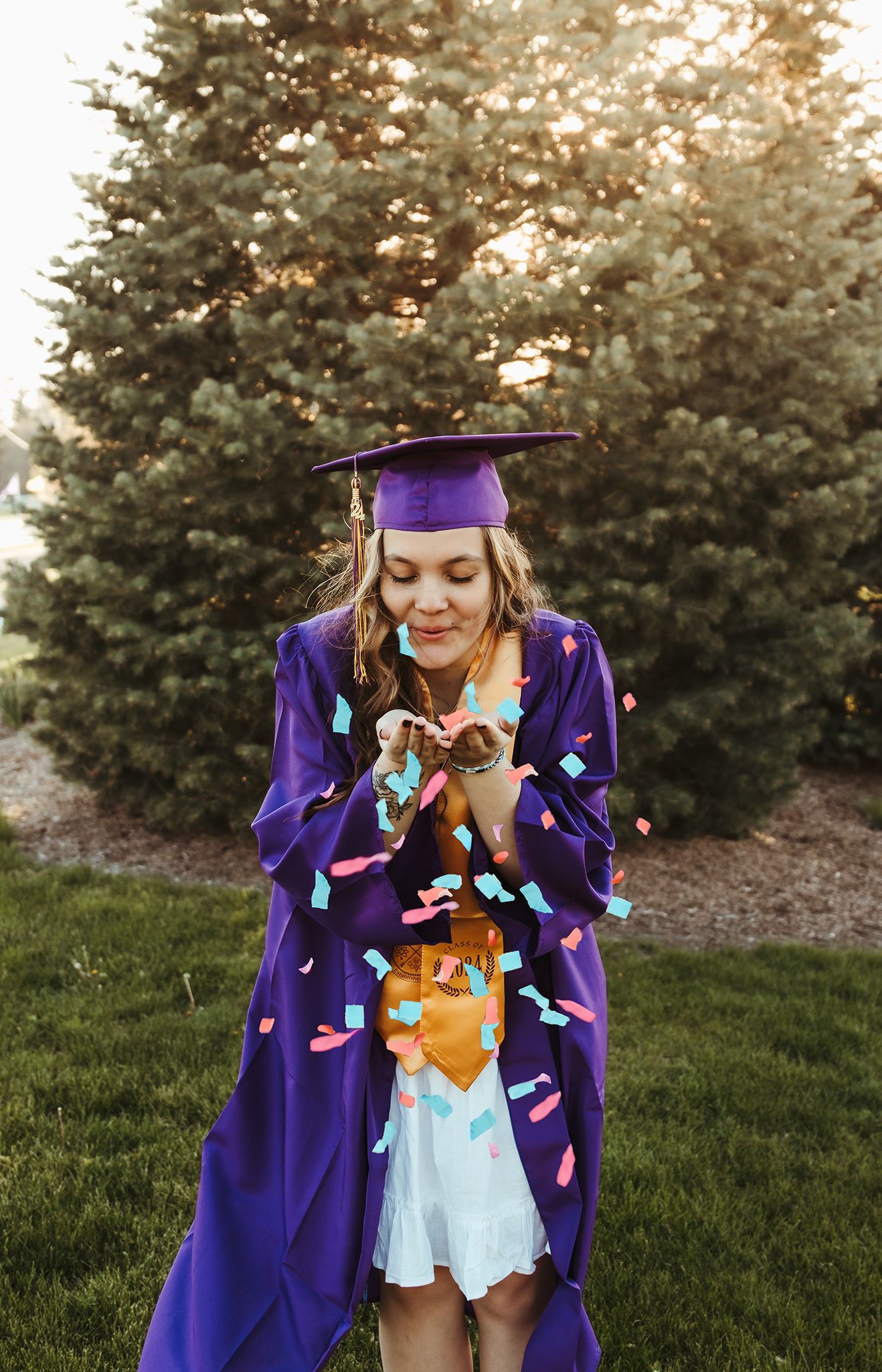 High school senior blowing confetti at the camera while wearing cap and gown for graduation photos