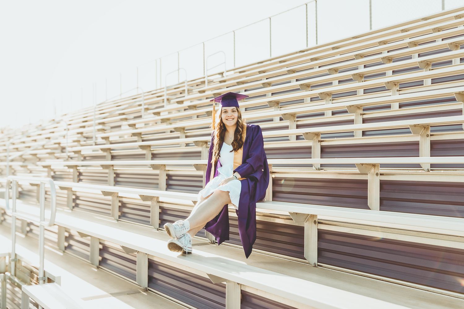 High school senior wears cap and gown while sitting in bleachers