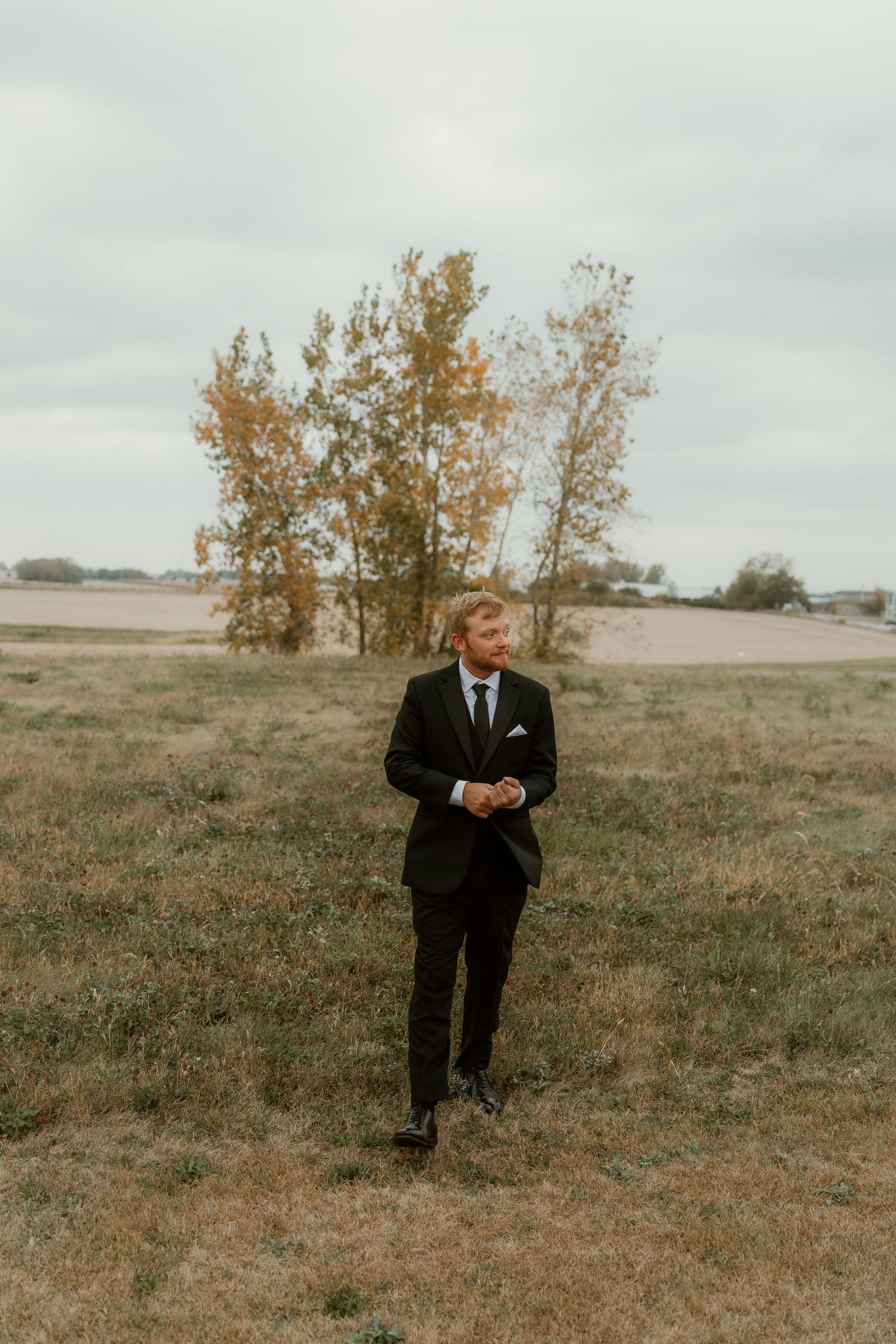 Groom takes a stroll through an open field during groom portraits