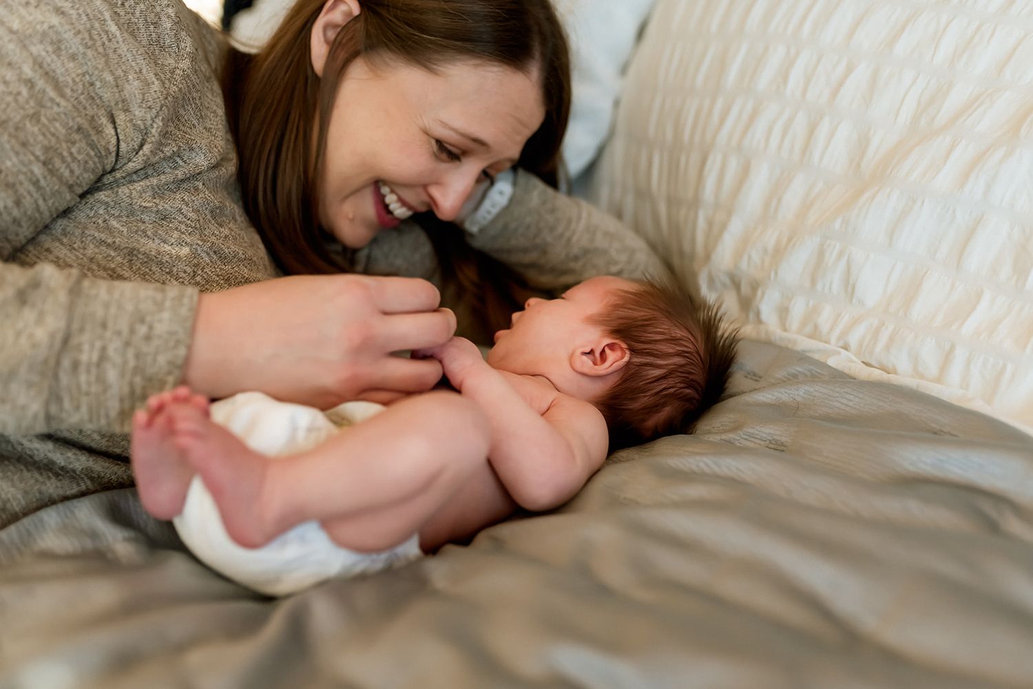 A tender moment between parent and newborn baby lying together on soft gray bedding.