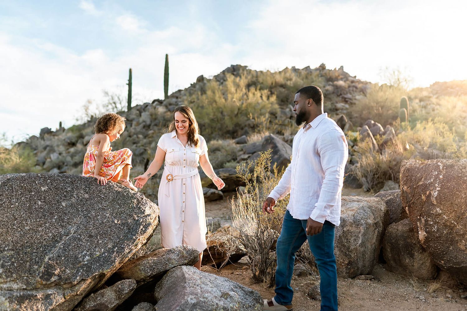 A couple in watches their daughter climb on rocks during a family photo session in Scottsdale.