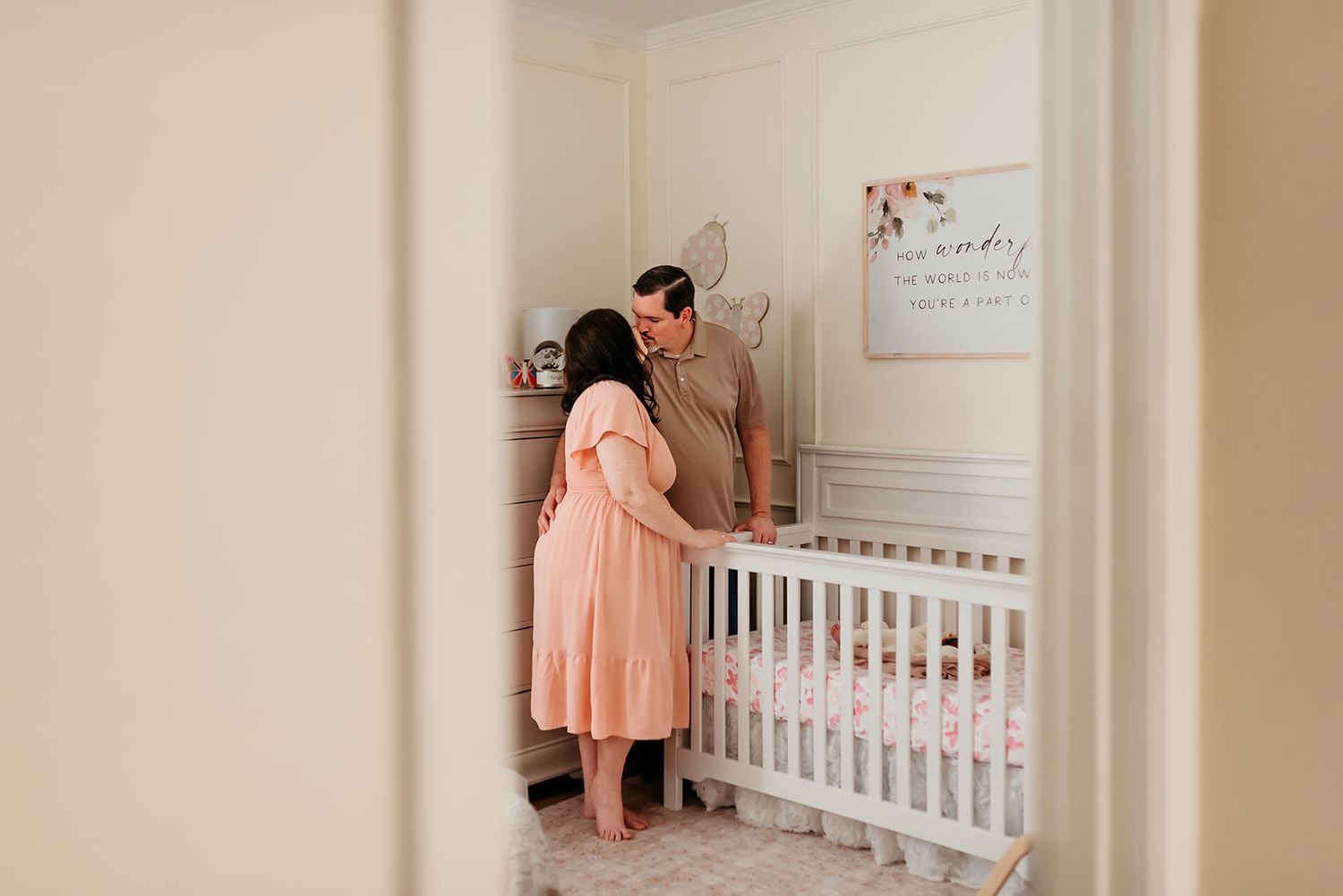 Parents stand together at a white crib in a nursery while kissing in their baby's room.