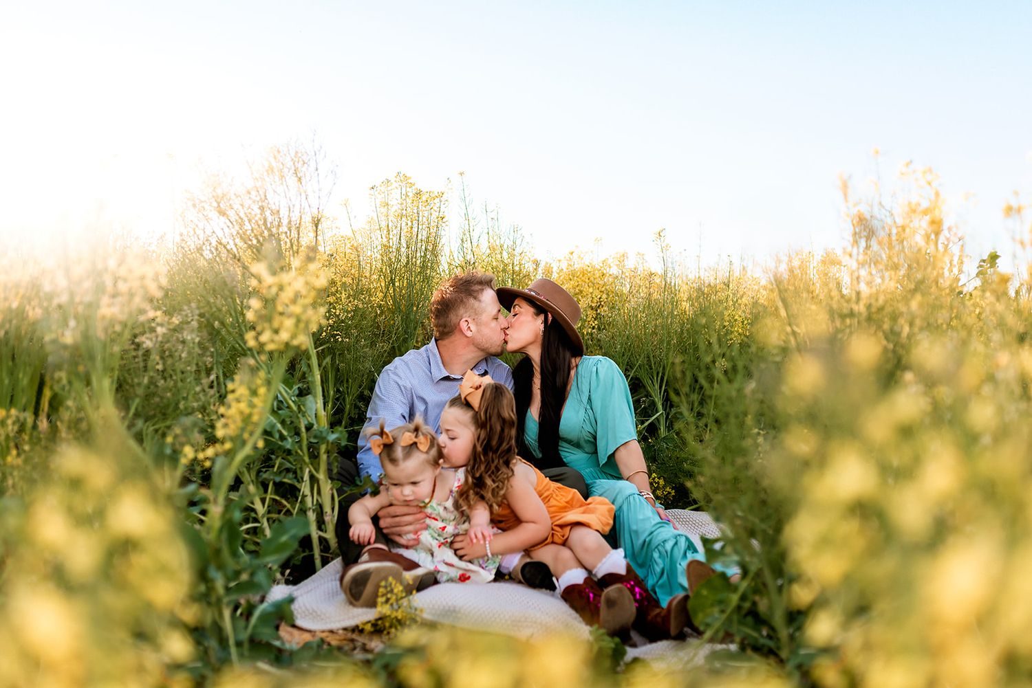 Family having a picnic together in a sunlit meadow with tall golden grass during sunset.