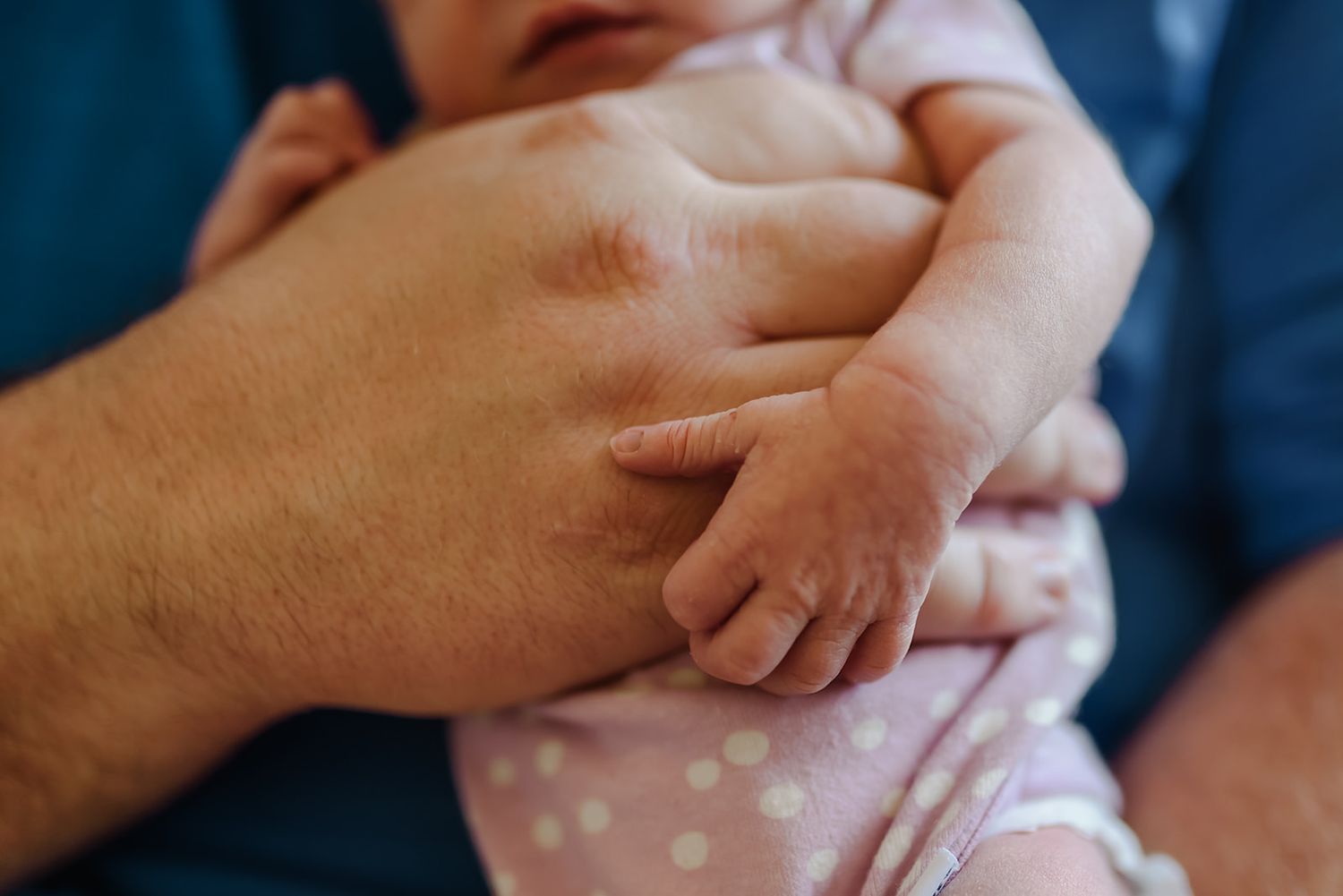 A close-up shot of a tiny newborn baby's hand grasping onto an adult's finger during a lifestyle newborn photo session.