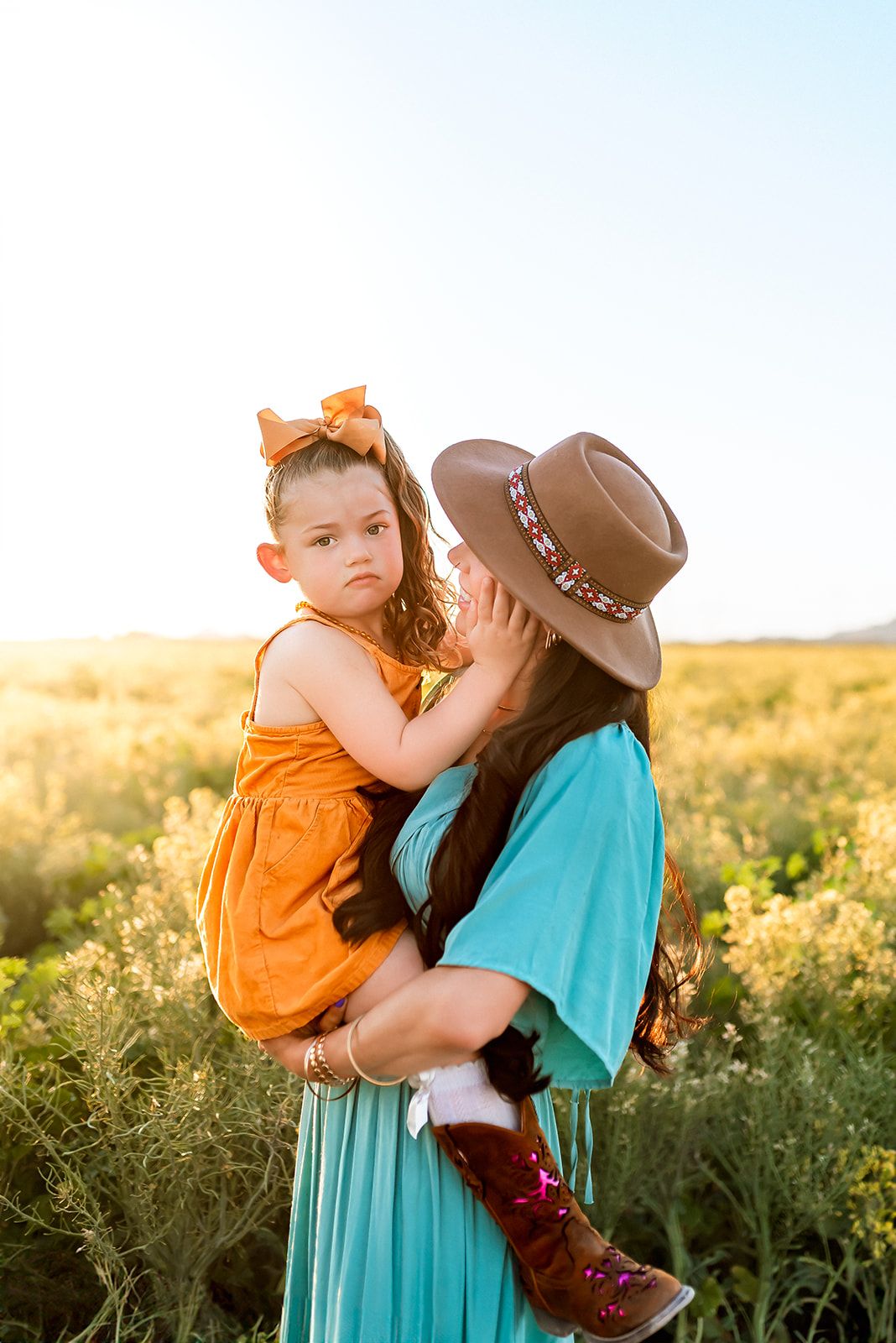 A touching moment in a golden field at sunset shows maternal affection in turquoise and orange against the warm Phoenix sky.
