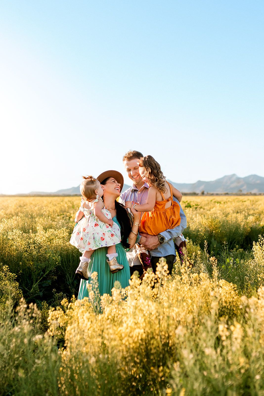 A family stands together in a golden field of wildflowers at sunset with mountains visible in the distance in Phoenix, AZ