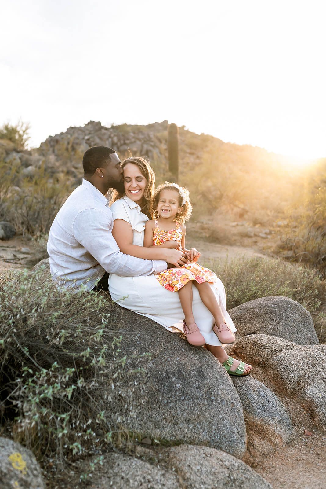 A family sits together on desert rocks at sunset in a peaceful outdoor portrait setting during a North Phoenix family photo session