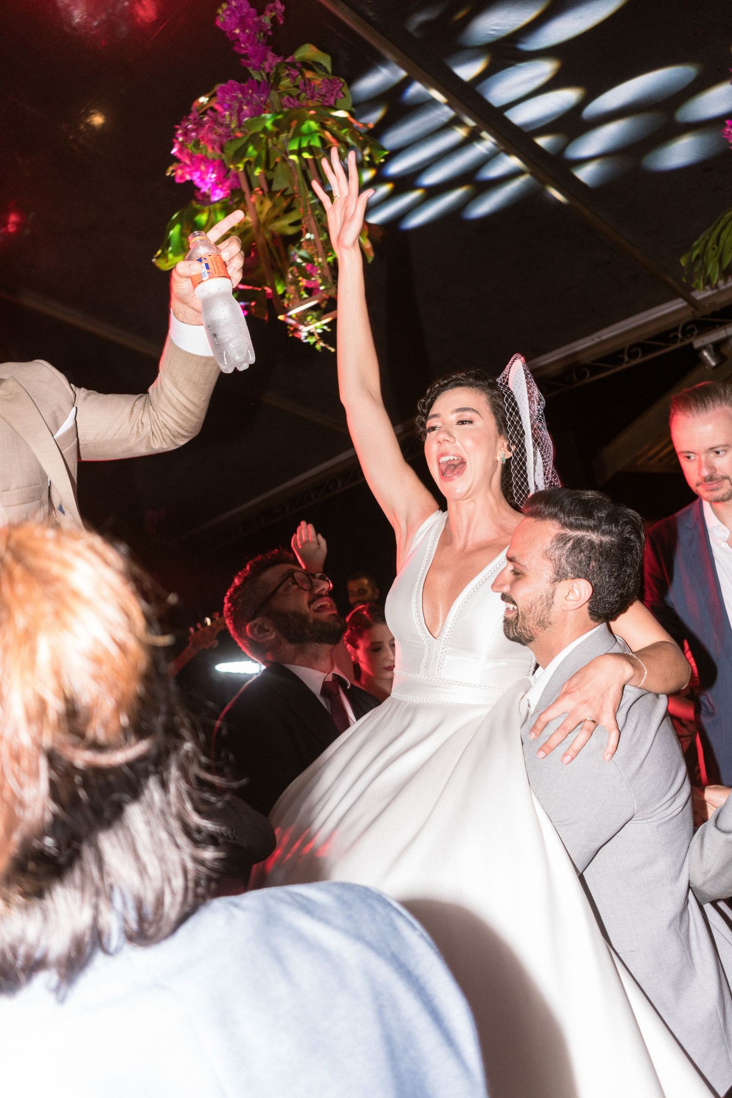 Noiva sendo levantada por amigos do noivo pra cantar e dançar juntos na festa de casamento