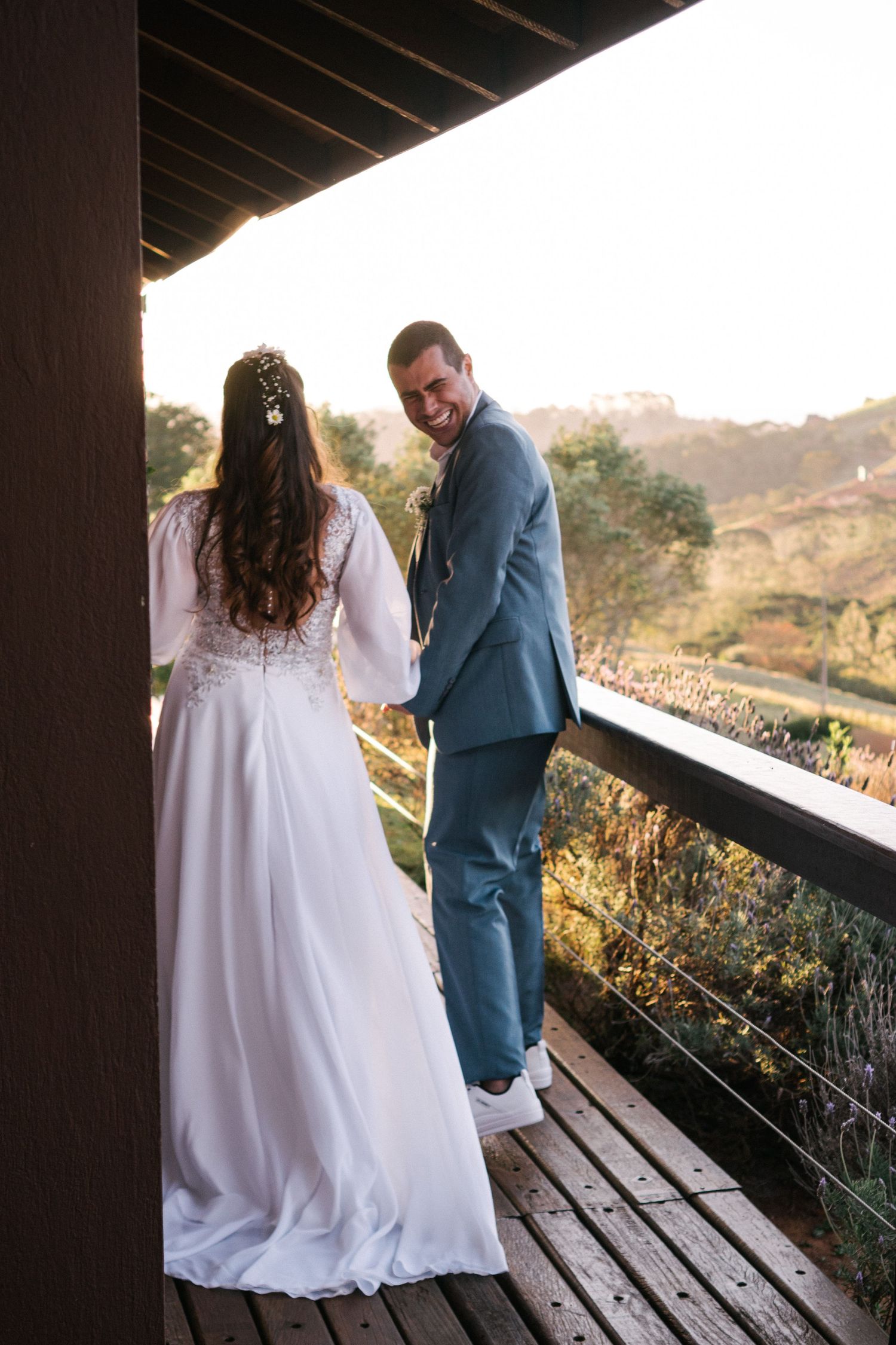 Casal de noivos compartilhando momento na varanda de madeira com vista para a paisagem montanhosa.