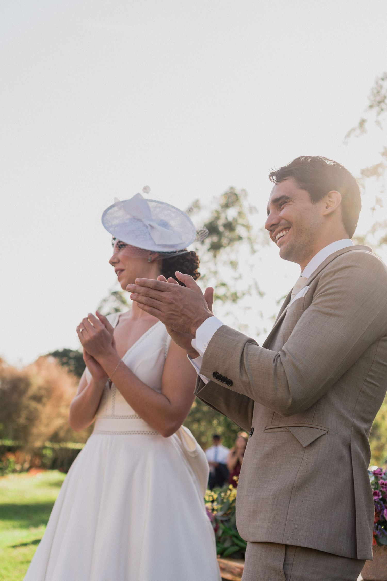 Noivos sorrindo juntos em um dia ensolarado, em um cenário de jardim durante a cerimônia do casamento ao ar livre