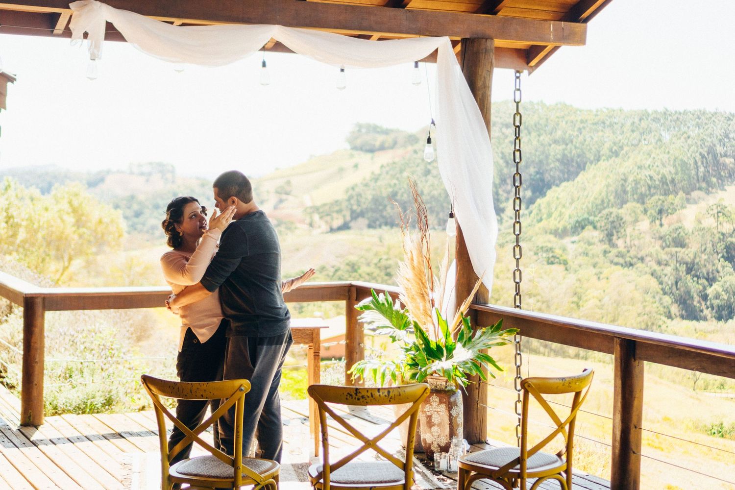 Um casal compartilha um momento de ternura em um deck de madeira com vista para as montanhas.