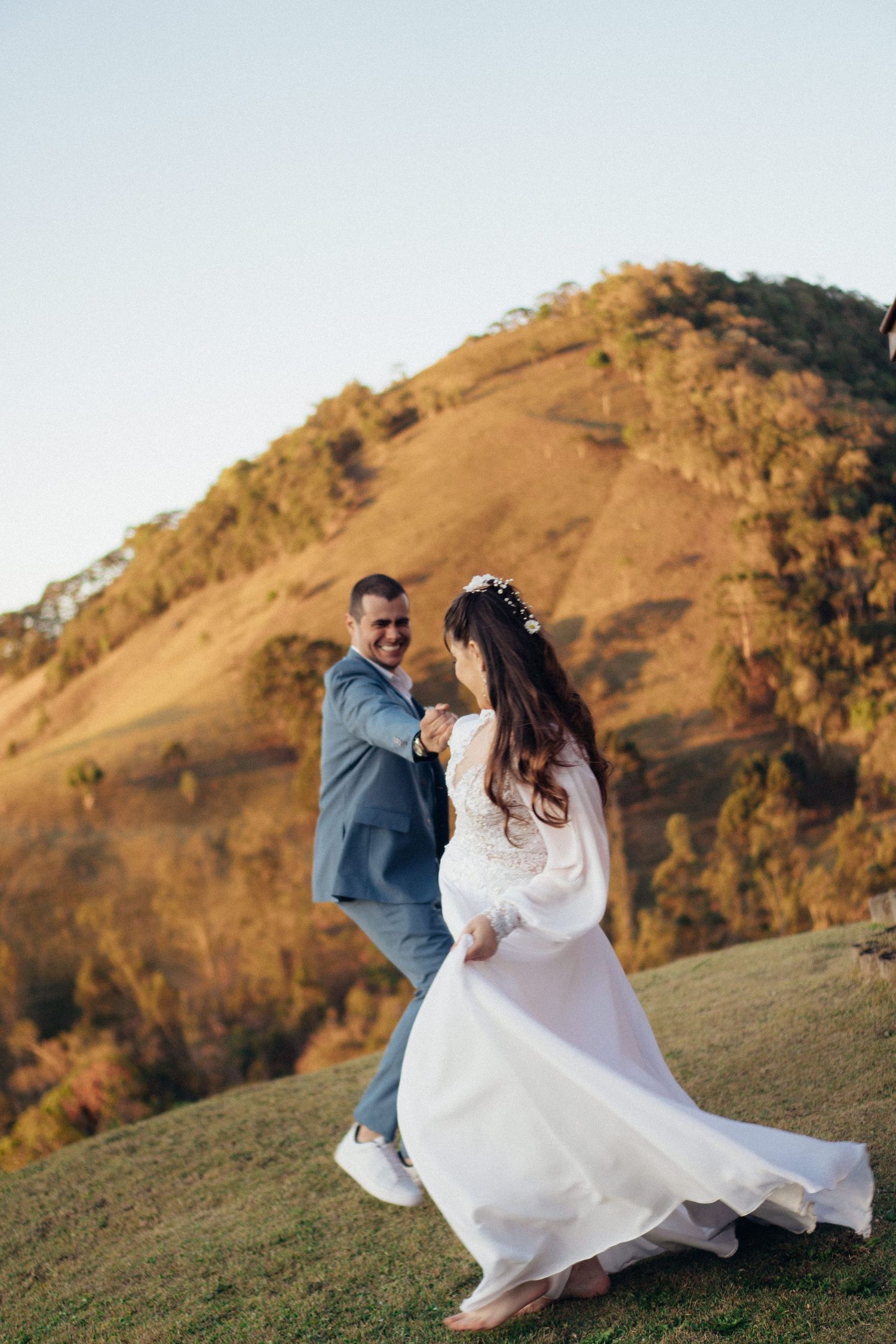 Um casal gira e dança junto no topo de uma colina com o vestido branco da noiva esvoaçando ao vento.