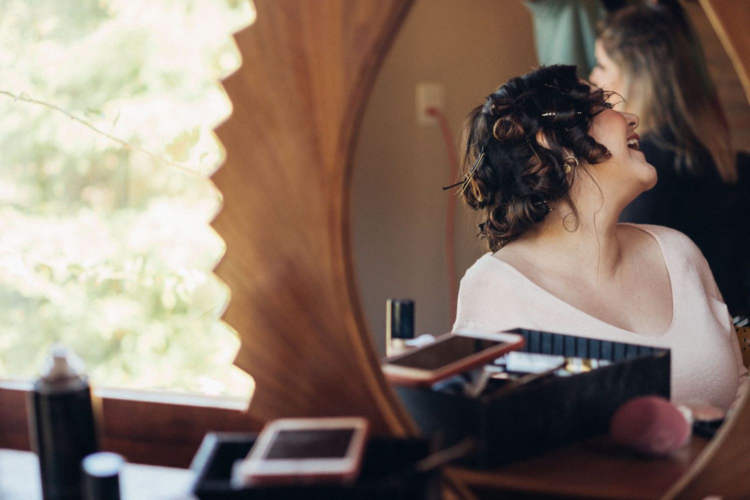 Reflection in mirror shows preparation scene with hair styling in progress.