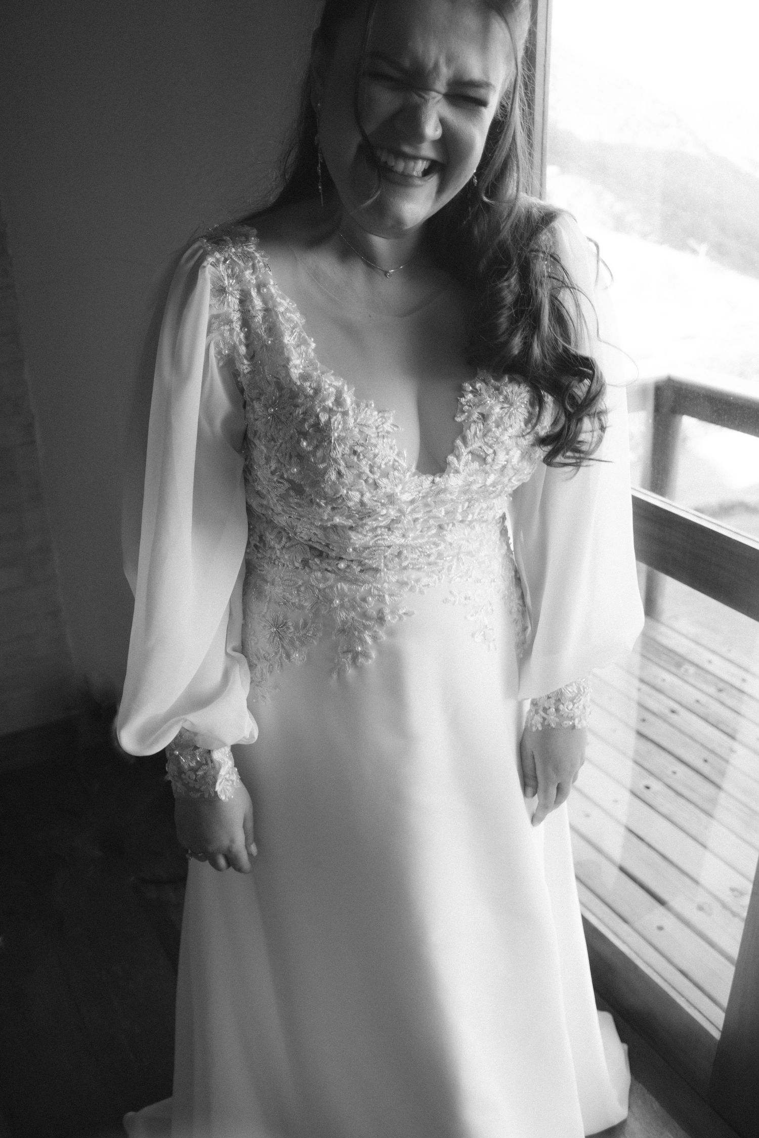A romantic long-sleeved wedding dress with delicate lace details and a plunging neckline in black and white photography.