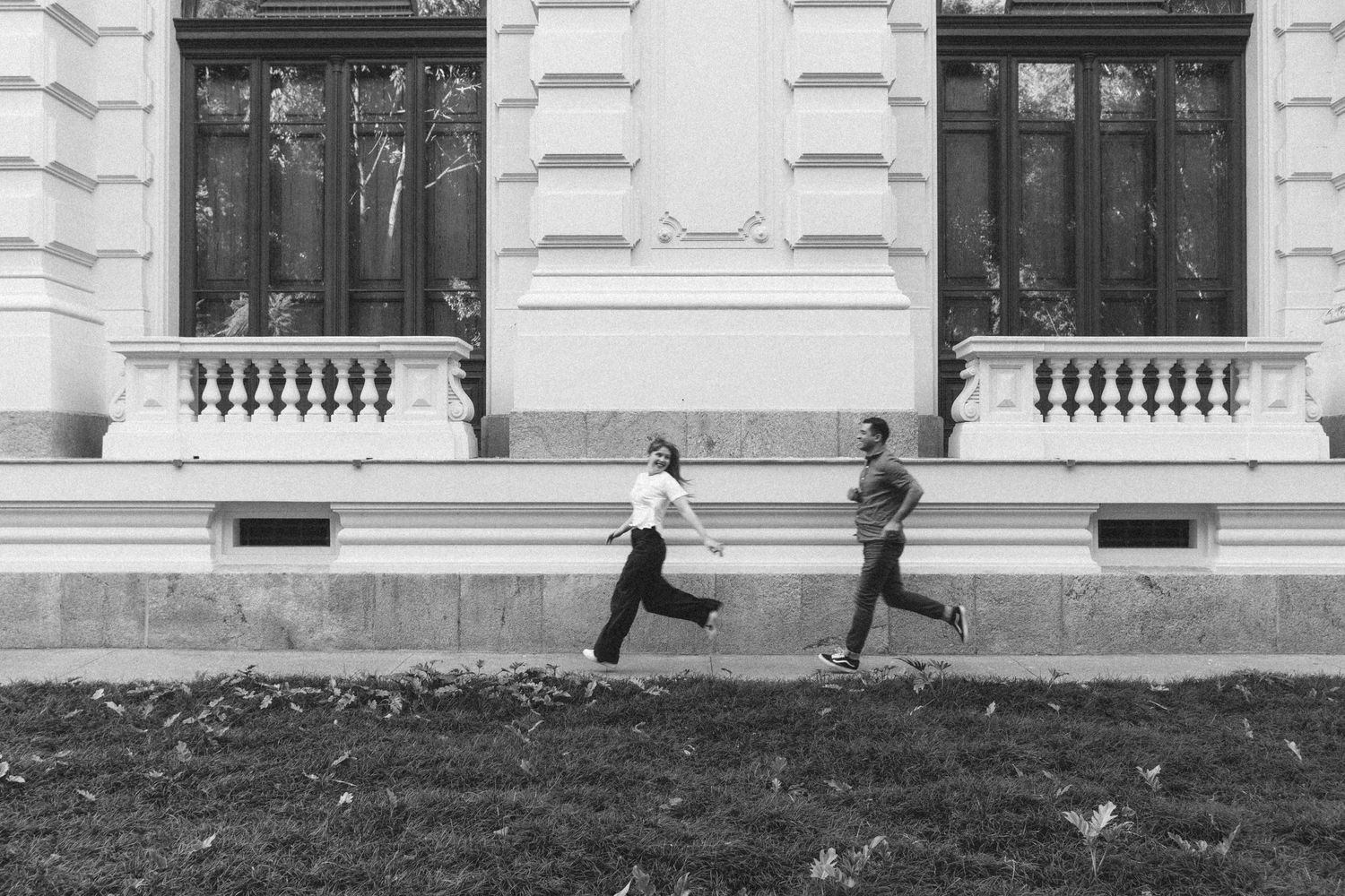 Casal corre da esquerda para a direita na foto em preto e branco © Clara e Matheus Fotógrafos de Casamentos