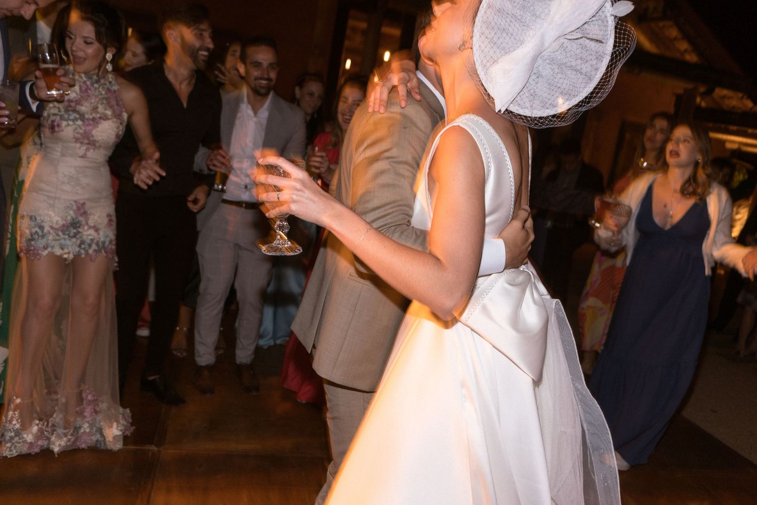 Convidados dançam e celebram na recepção noturna enquanto a noiva, em vestido branco, gira com o noivo na pista de dança iluminada