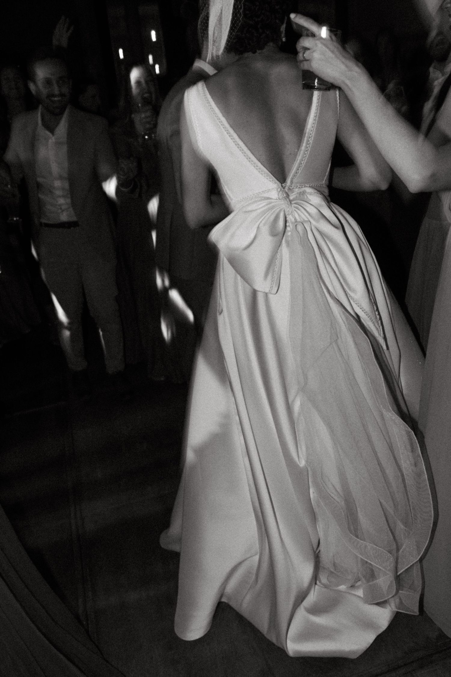 Fotografia em preto e branco destaca um elegante vestido de noiva em cetim branco com detalhe de laço durante a recepção de casamento