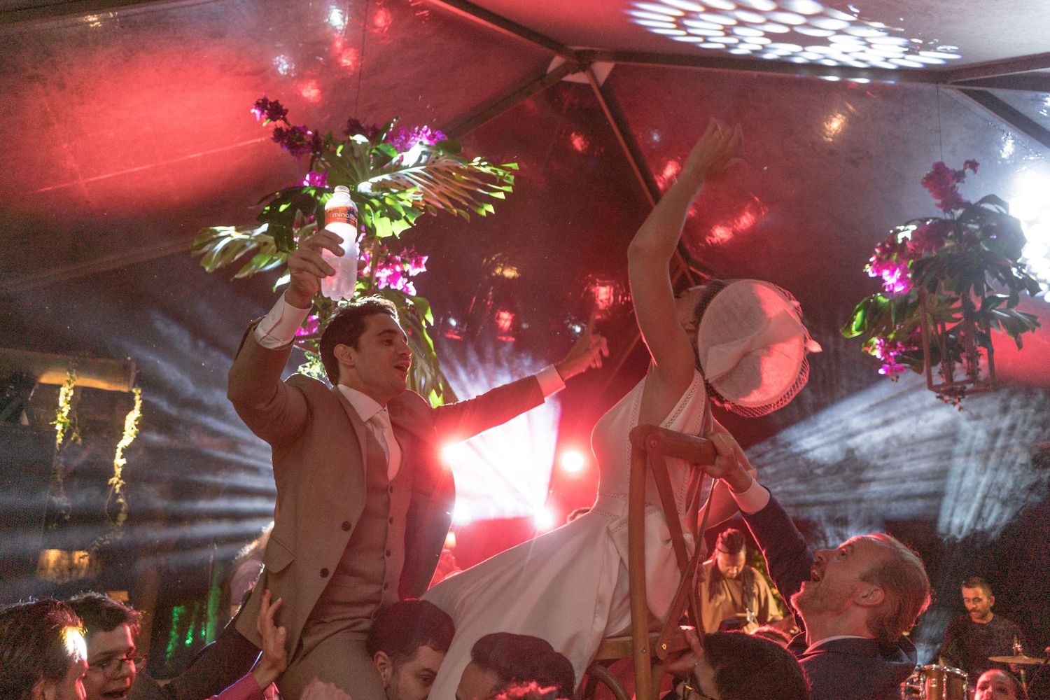 Noivos durante festa de casamento elevados em cadeiras pelos amigos e convidados, cantando e rindo juntos, fotografado por Clara e Matheus