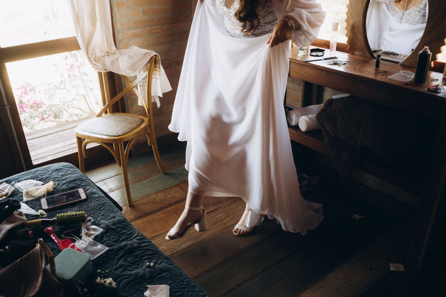 Detail shot of a flowing white wedding dress hem against wooden floorboards.
