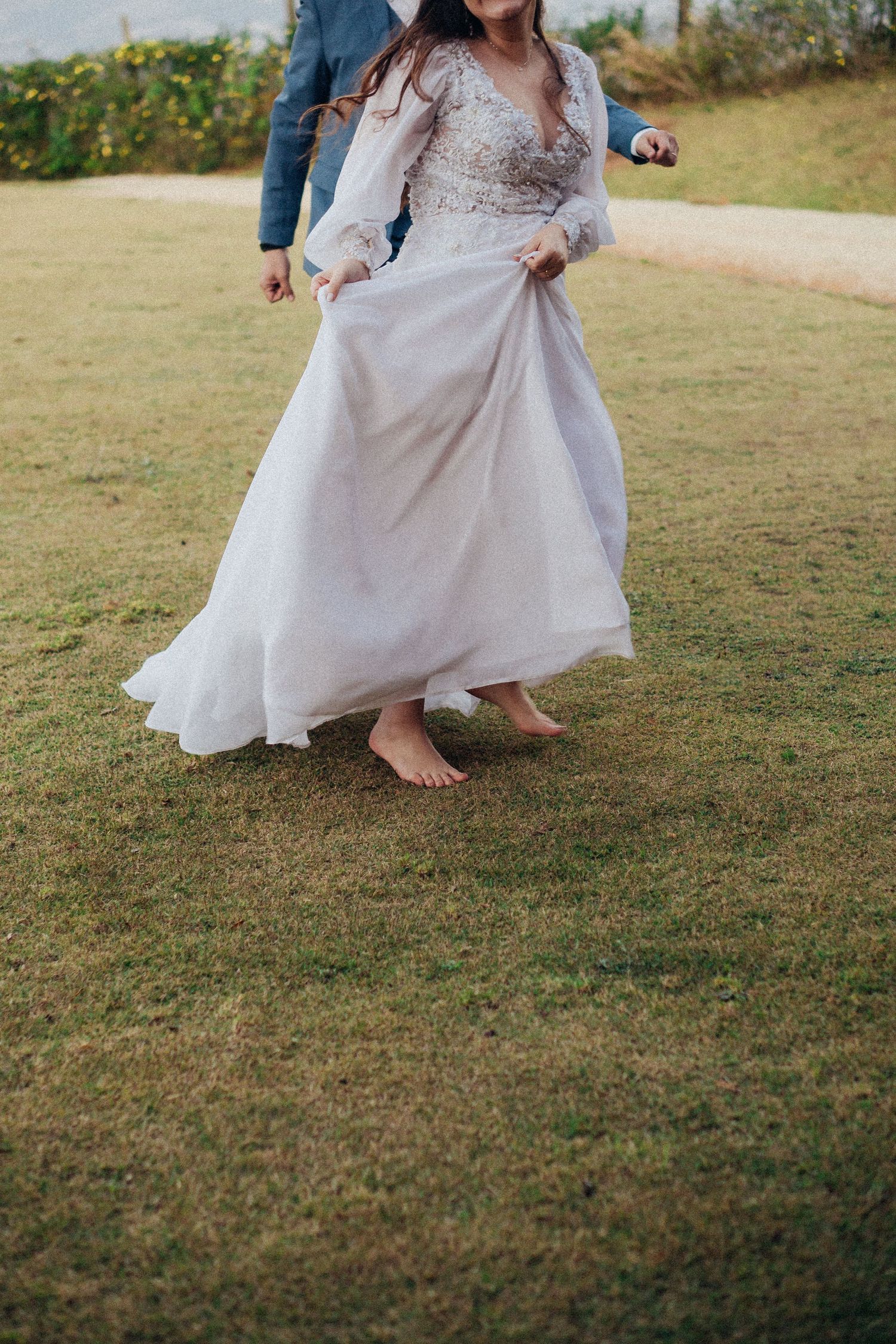 A bainha esvoaçante de um vestido de noiva branco move-se graciosamente sobre a grama verde enquanto quem a veste dança.
