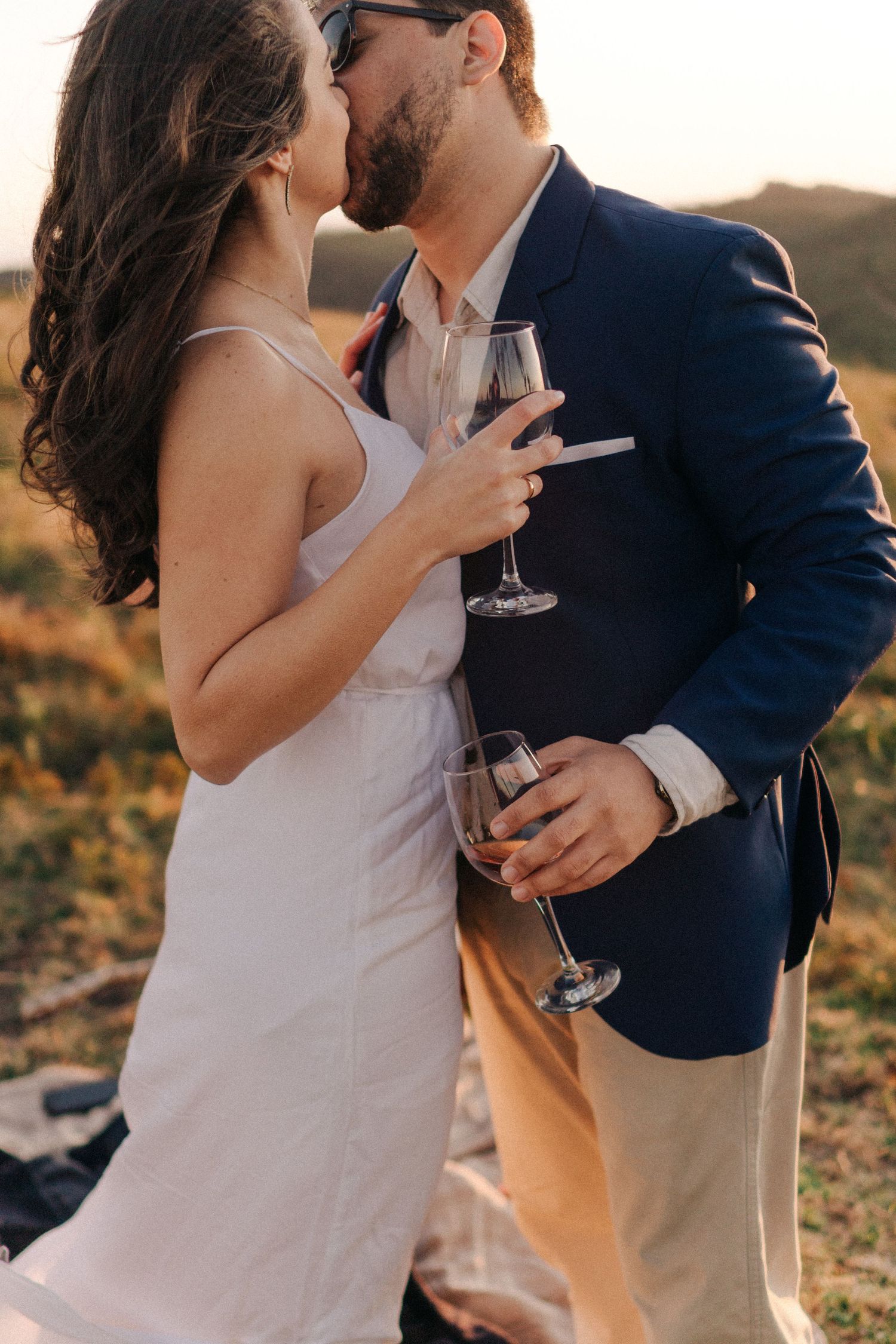 Couple holds wine glass in the sunset while kissing. Picture by Matteo and Clara, couple and wedding photographers in Fl