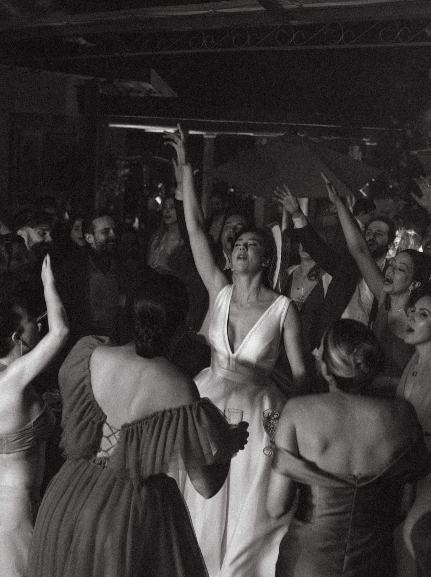 Noiva rodeada de amigas cantando juntas durante a festa de casamento, momento descontraído em que todos estão curtindo a música com as mãos