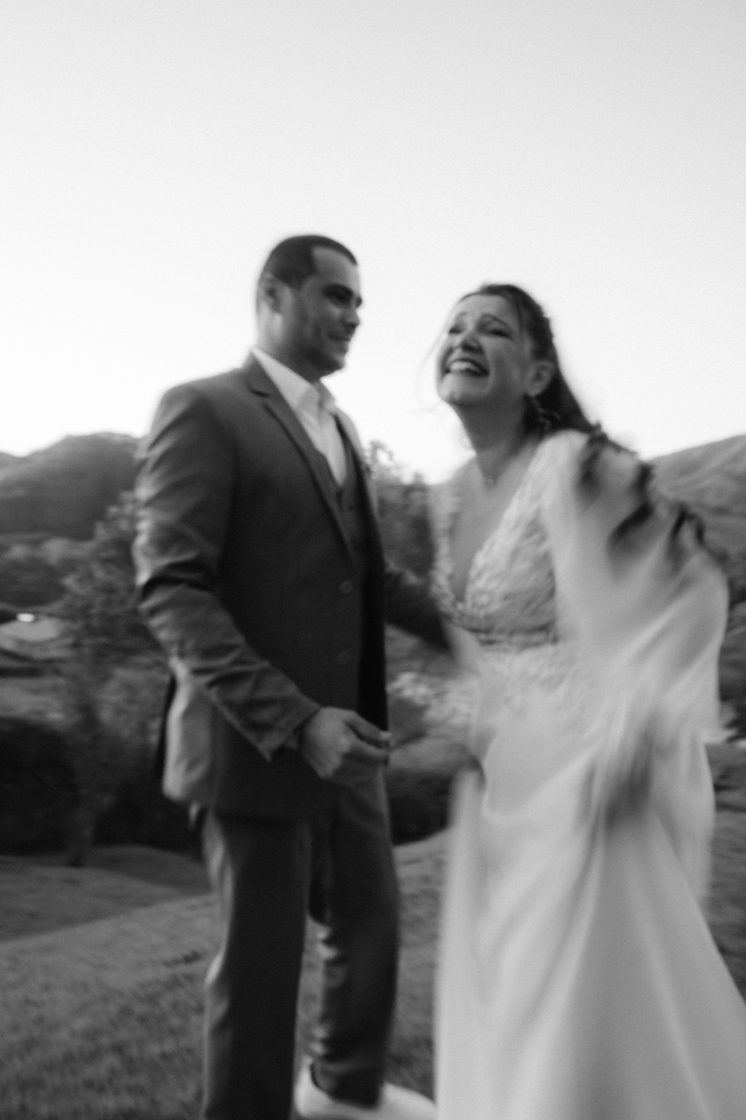 Foto em preto e branco de noivos rindo juntos durante retratos de casamento ao ar livre.