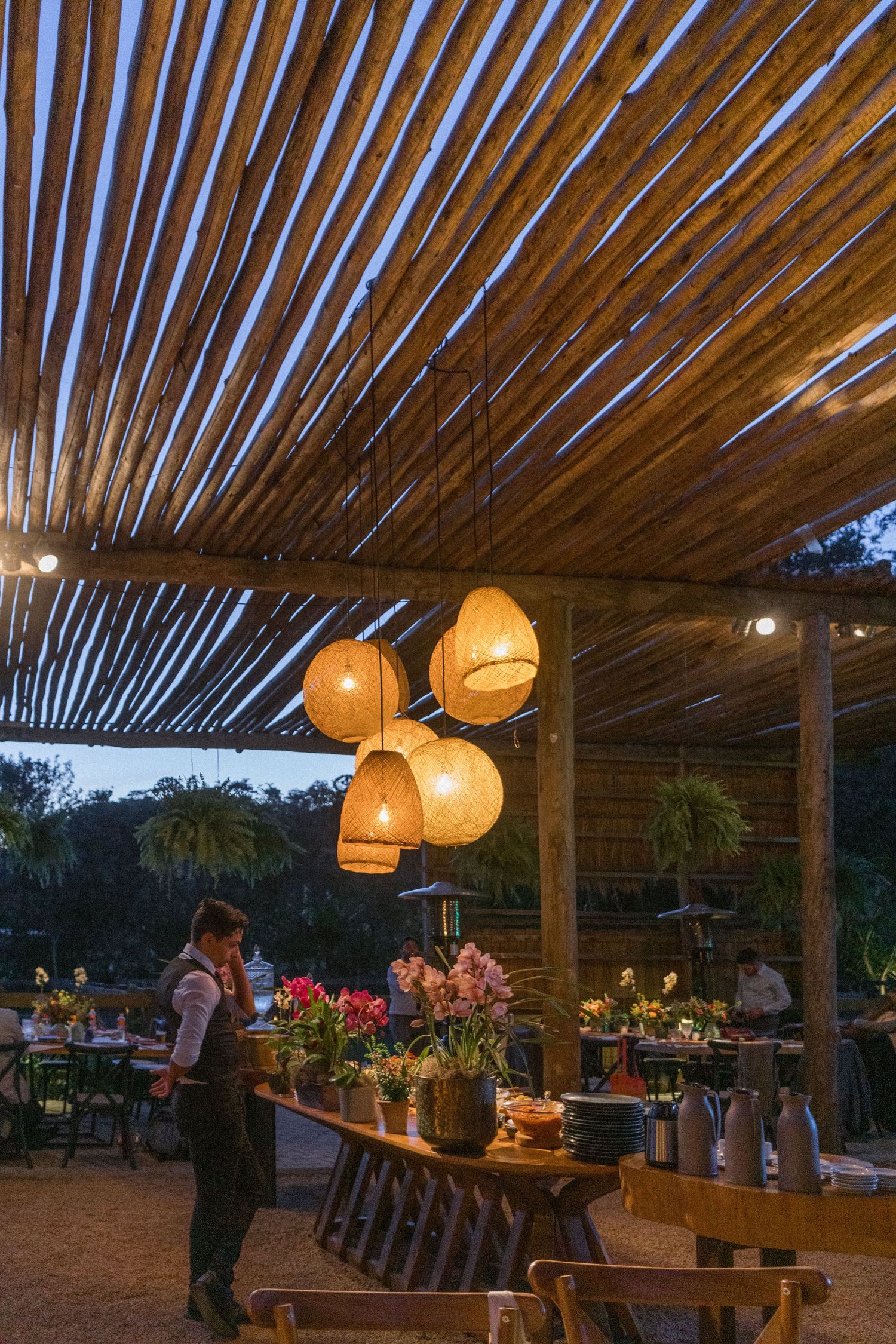 Decoração rústica de casamento com uma cobertura de bamboo, e mesa posta com flores coloridas no final da tarde