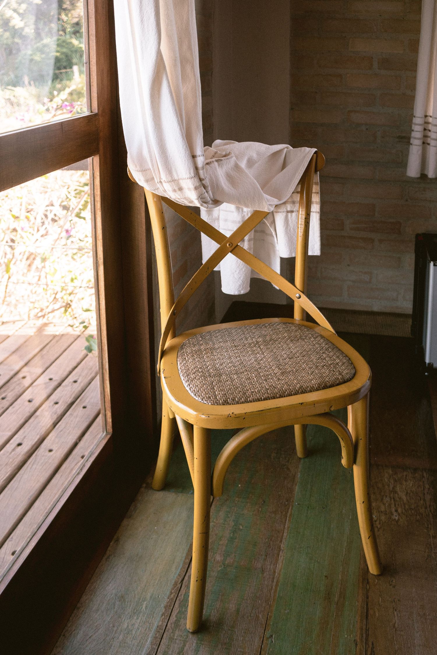 Vintage wooden chair with woven seat and white fabric draped over it near a window.