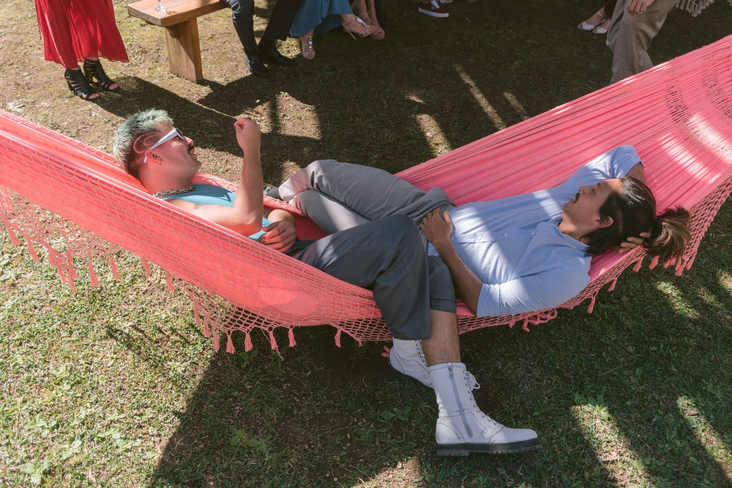 Dois convidados relaxam juntos em uma rede rosa em dia ensolarado, em cenário ao ar livre durante a cerimônia de casamento