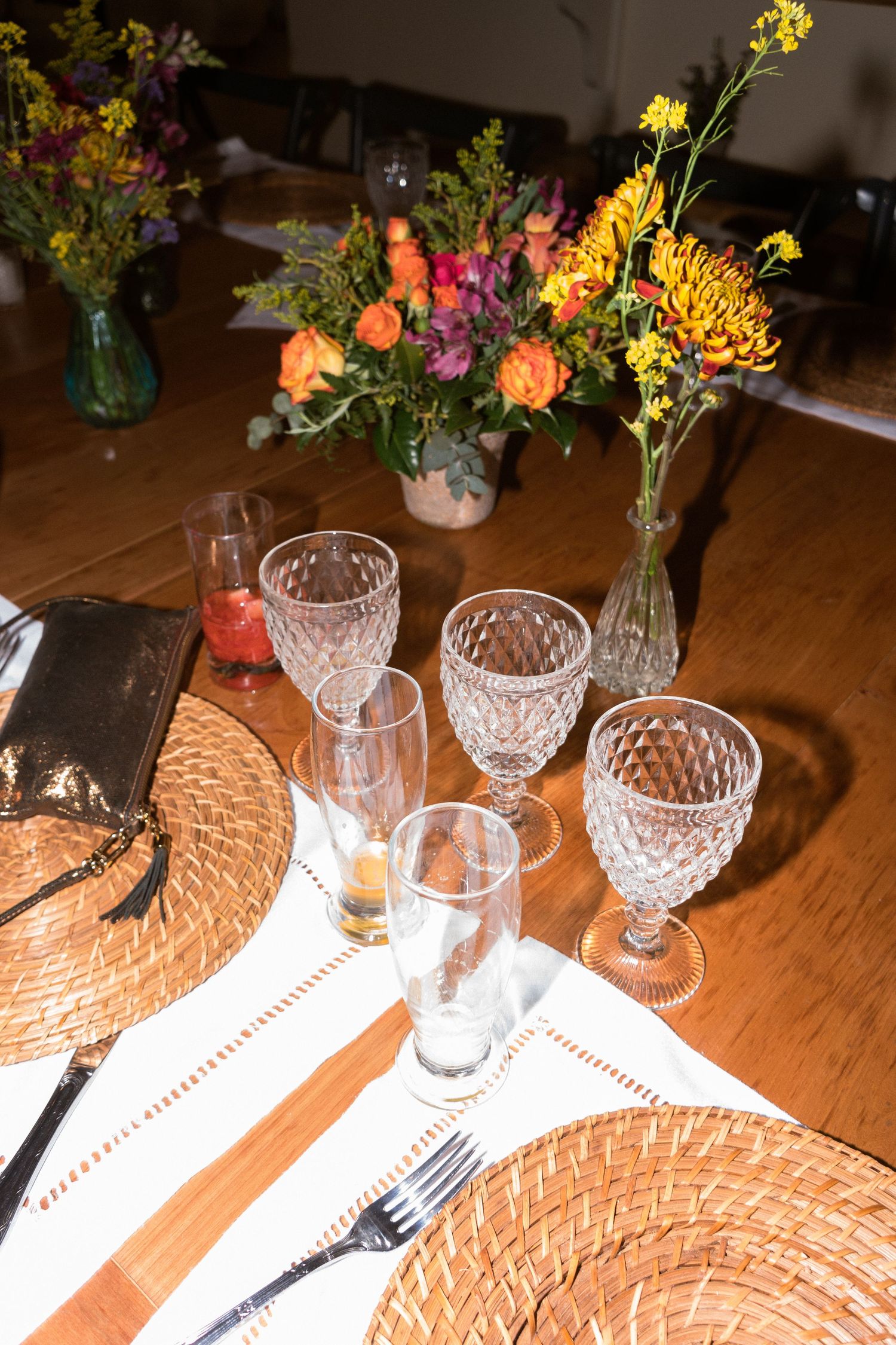 Mesa elegantemente decorada com sousplats de palha, taças de cristal e arranjos florais coloridos como centro de mesa de festa de casamento
