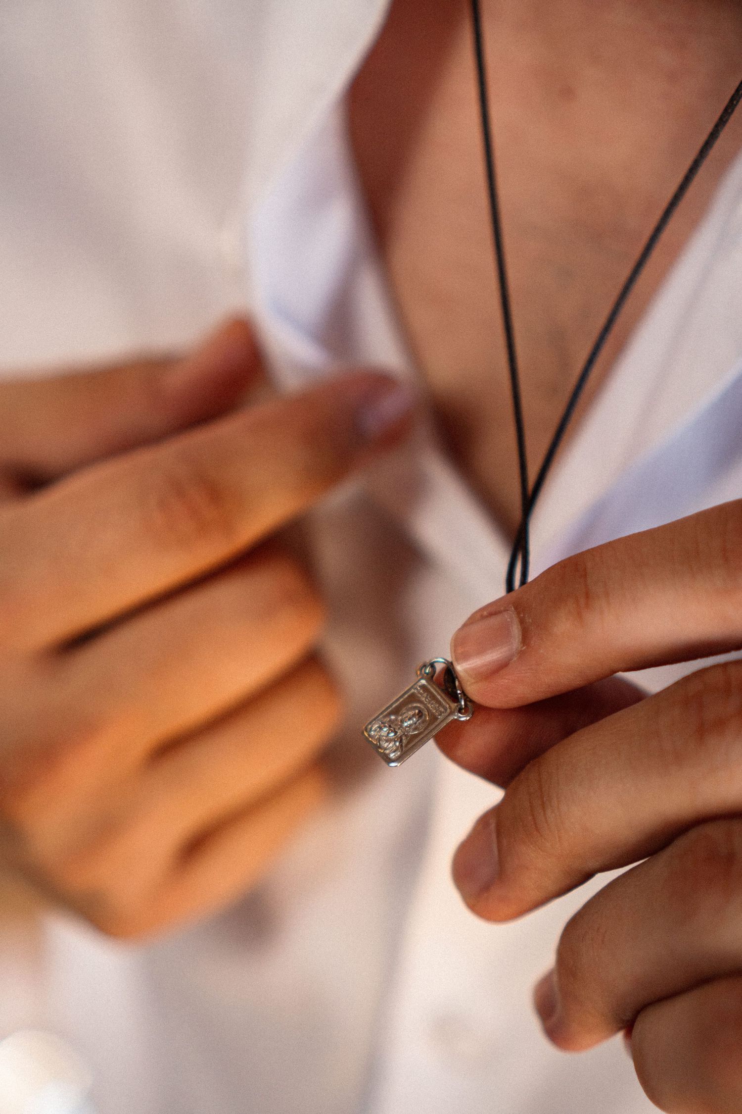 Close-up of hands holding a delicate necklace with ring pendant in warm lighting.
