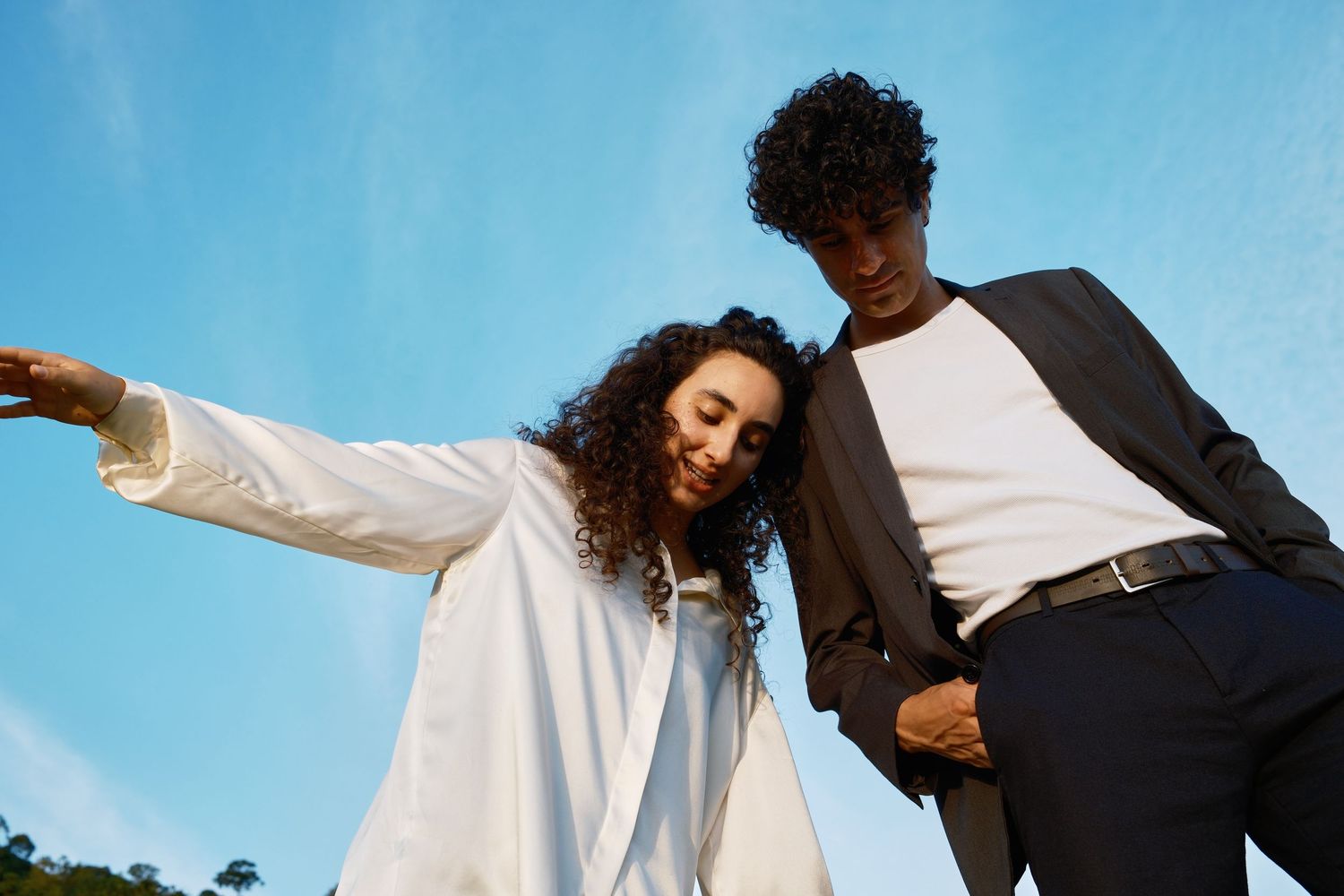 Casal vestido de branco e preto dançando junto contra um céu azul em série de fotos artísticas.